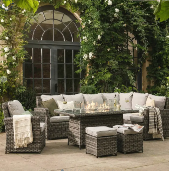 an outdoor sofa set with chairs and a fire pit table in rattan in front of an arched door with roses climbing on the walls