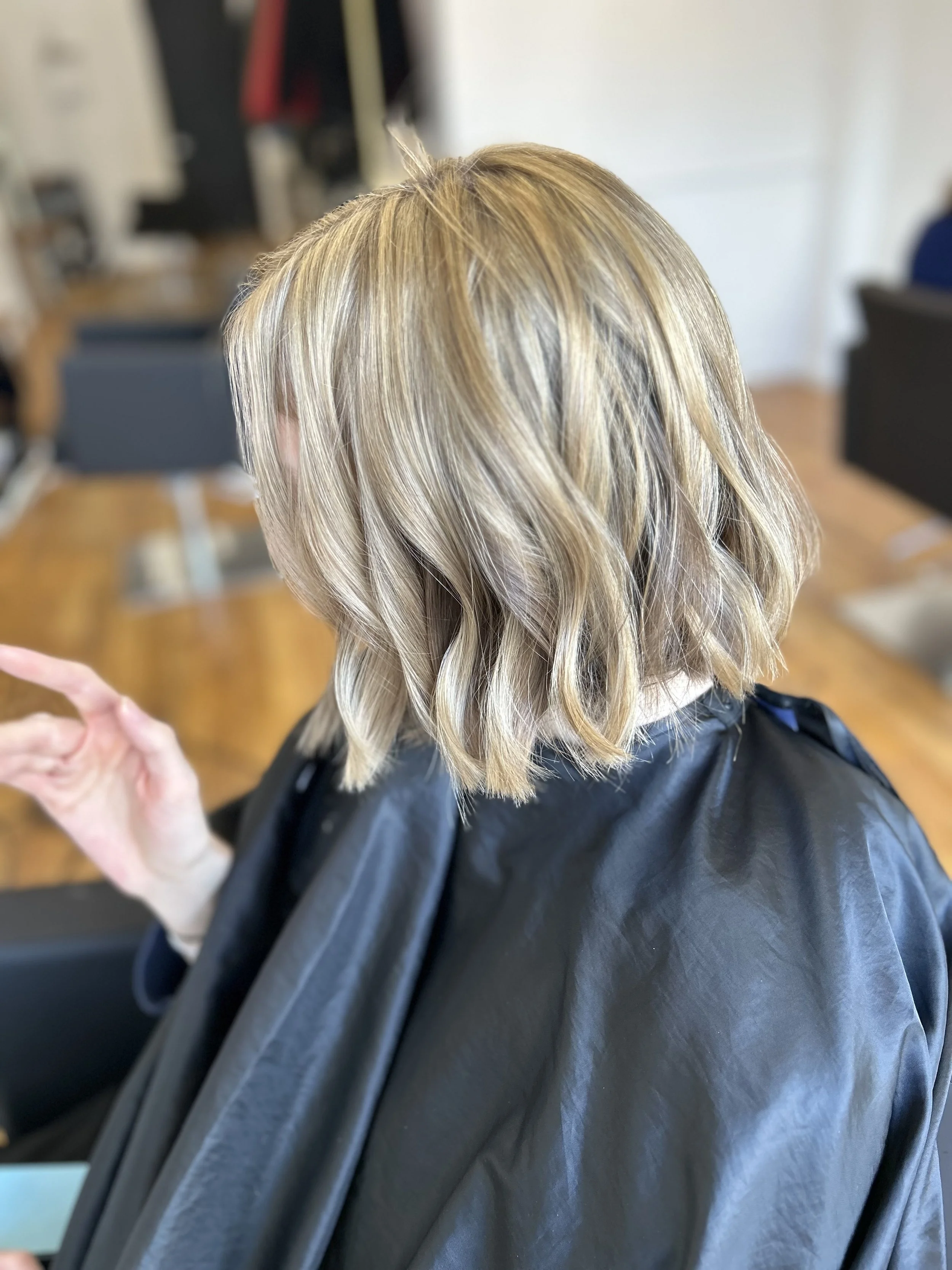 This hairstyle features a soft, luminous blonde with natural dimension and gentle layering. The face-framing layers create a flattering shape, while the smooth finish and light movement give the hair an elegant, effortless feel. A clean and timeless 