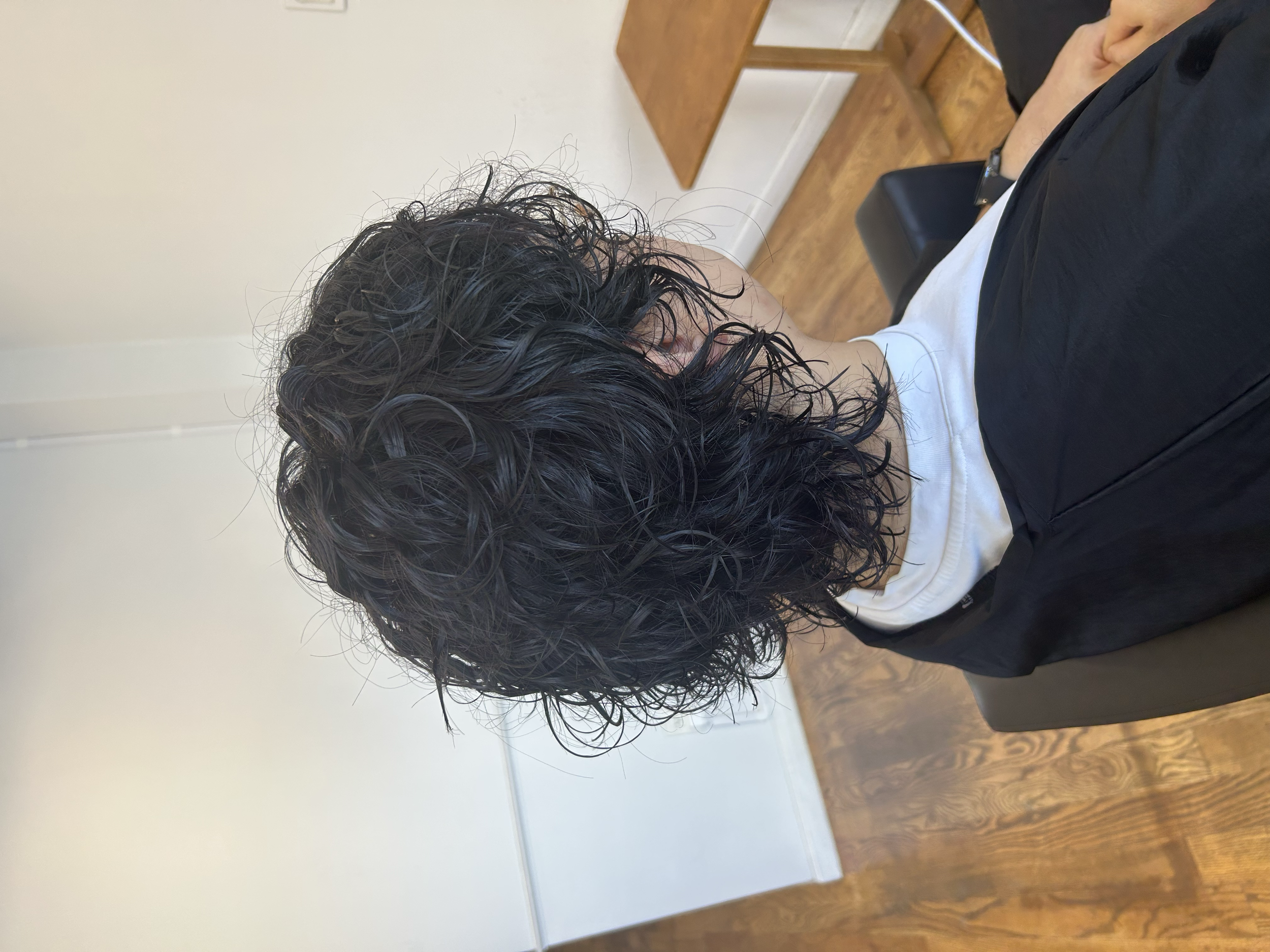 Back view of a layered wave perm with defined curls and volume on medium-length dark hair at U&K Salon.