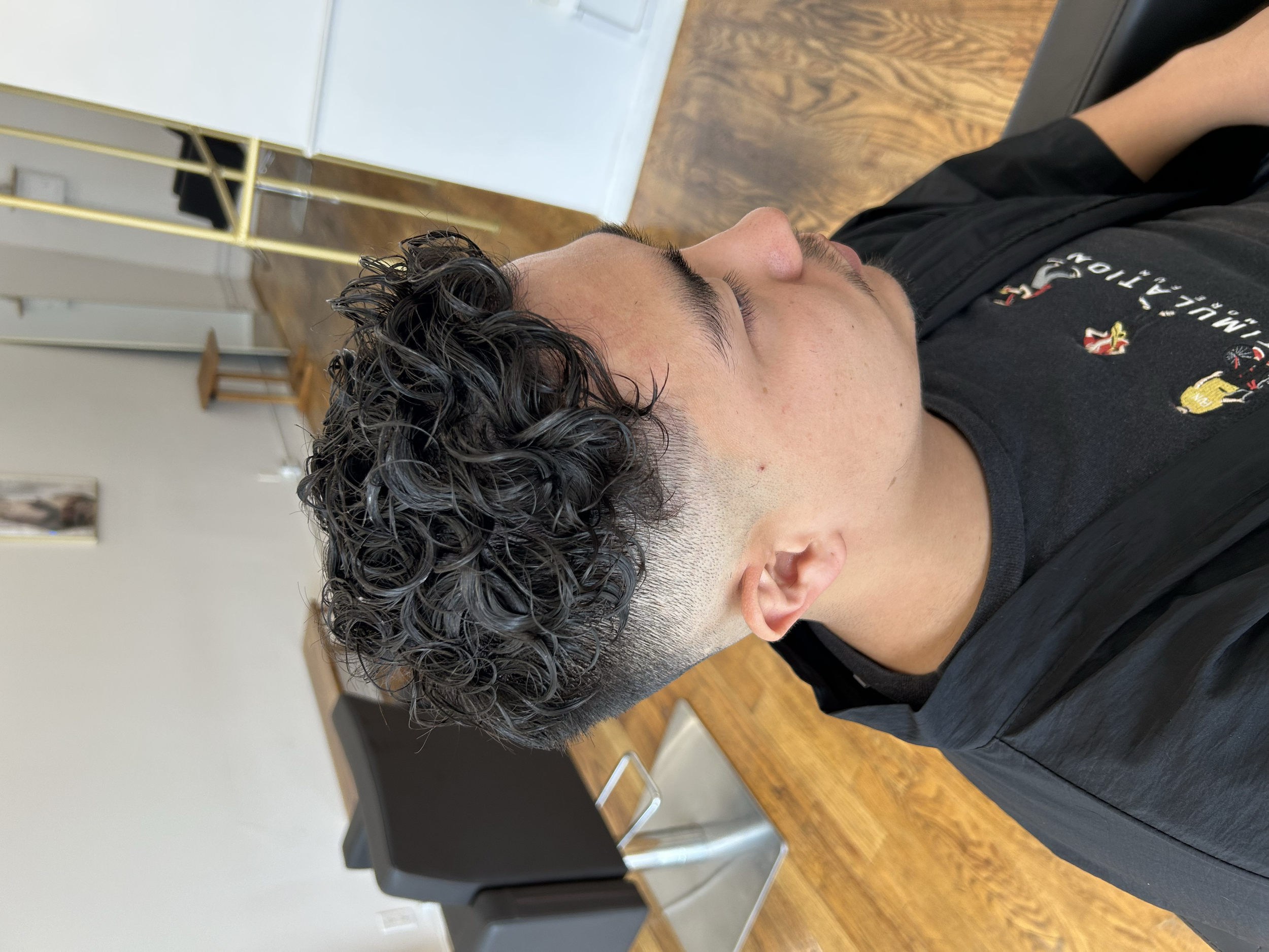Short men's curly wave perm with defined curls and a clean fade at U&K Salon in Brooklyn.