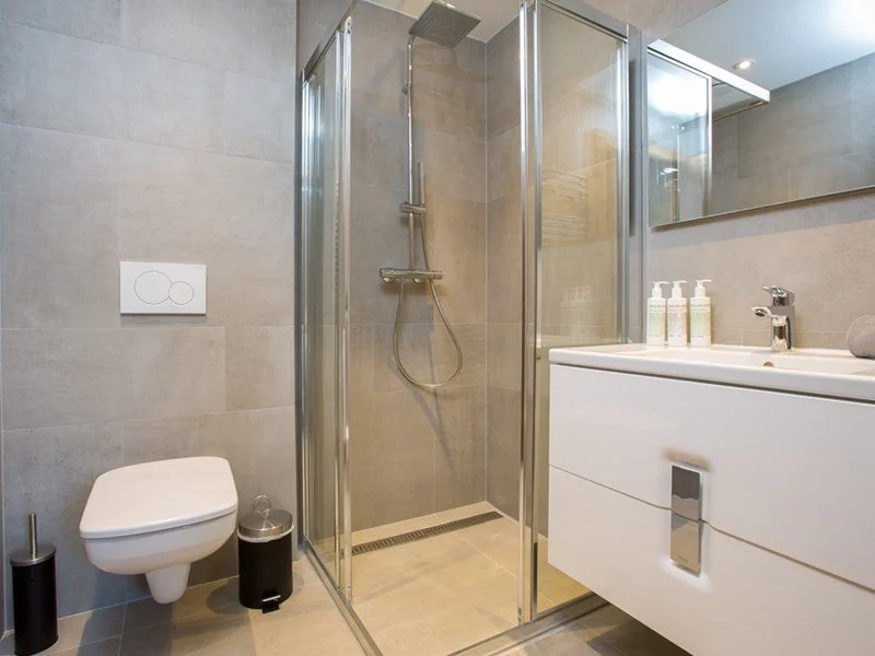 Modern bathroom with a corner shower, white toilet, and a white vanity with toiletries