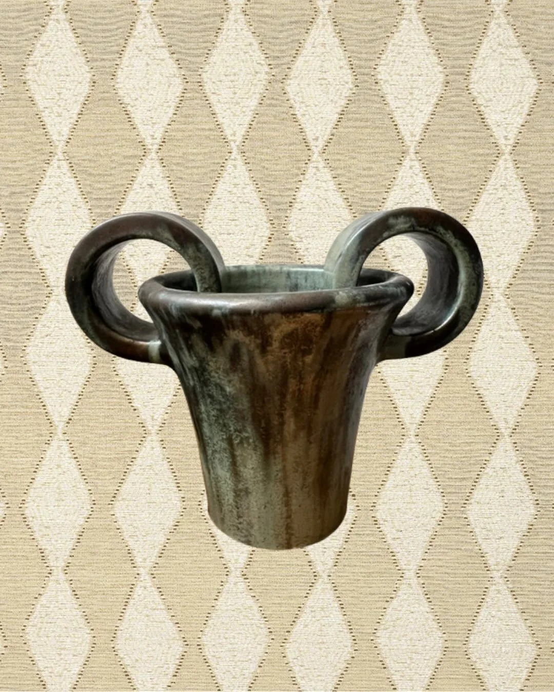 Vase sculptural en c&eacute;ramique &eacute;maill&eacute;e
Une pi&egrave;ce &agrave; la pr&eacute;sence forte, presque tot&eacute;mique.
Ses anses en volutes et sa patine profonde &eacute;voquent les rituels antiques autant que l&rsquo;audace contemp