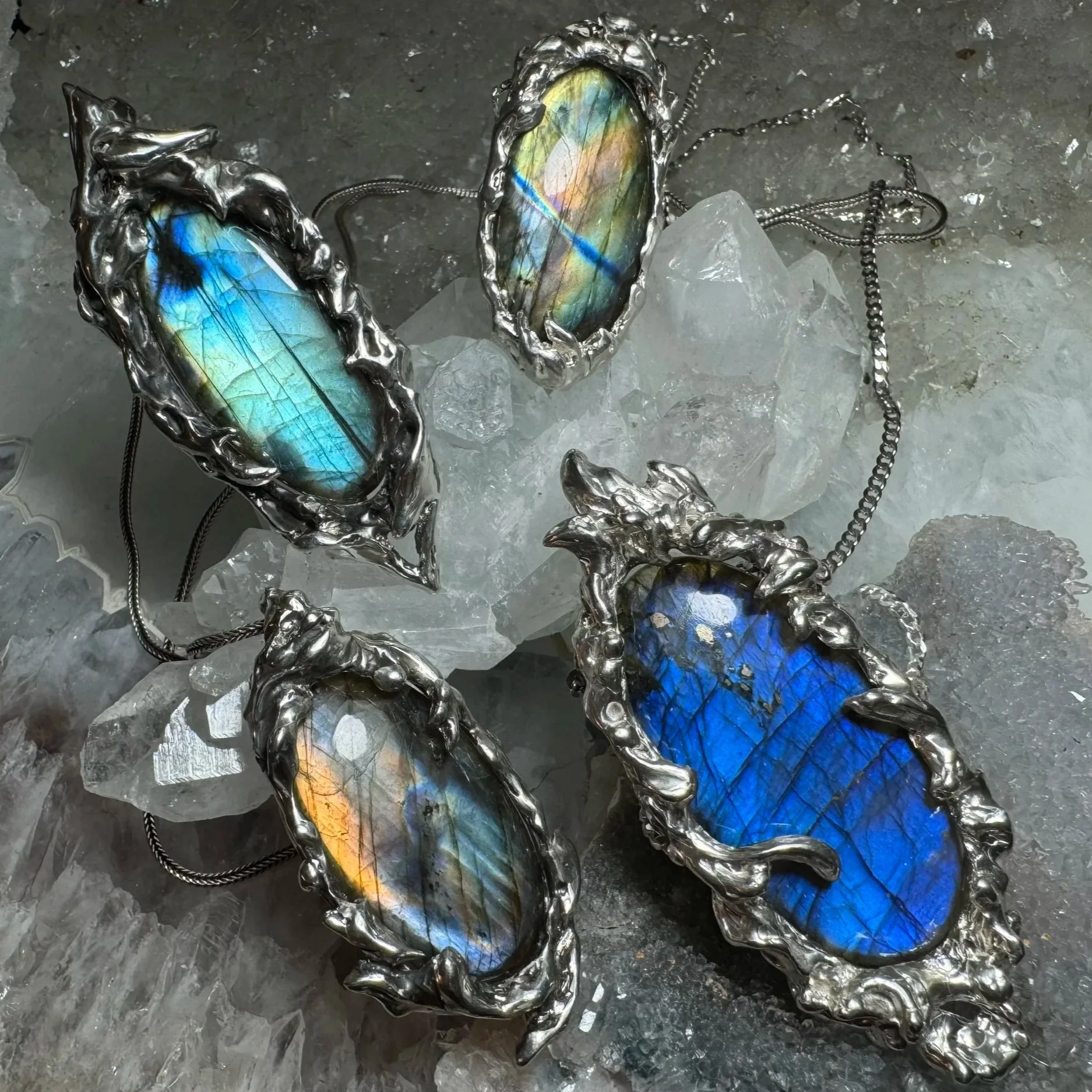 Four pieces of jewelry featuring labradorite stones with metallic silver settings, on a bed of clear quartz crystals.