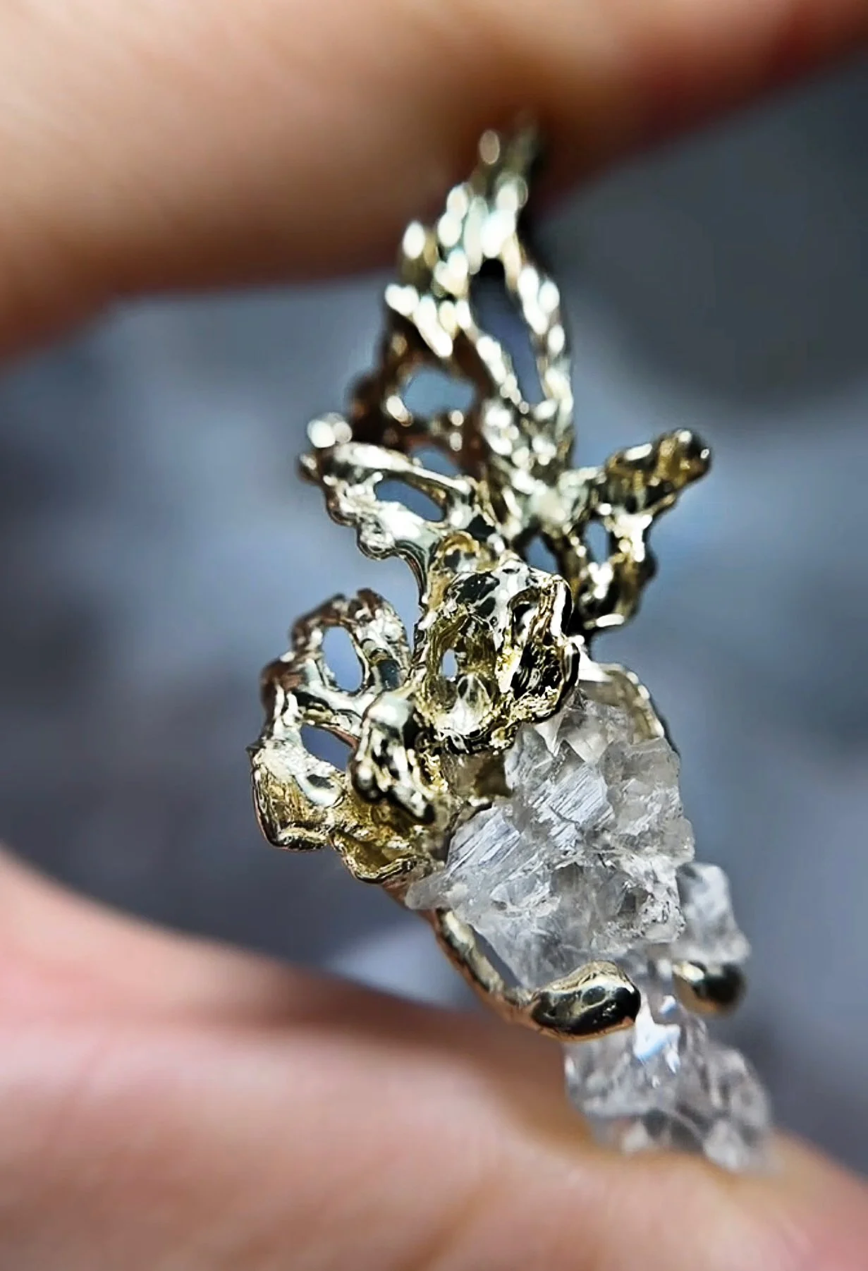 Close-up of a gold ring featuring an intricate, openwork floral design and a large, clear raw crystal at its center.