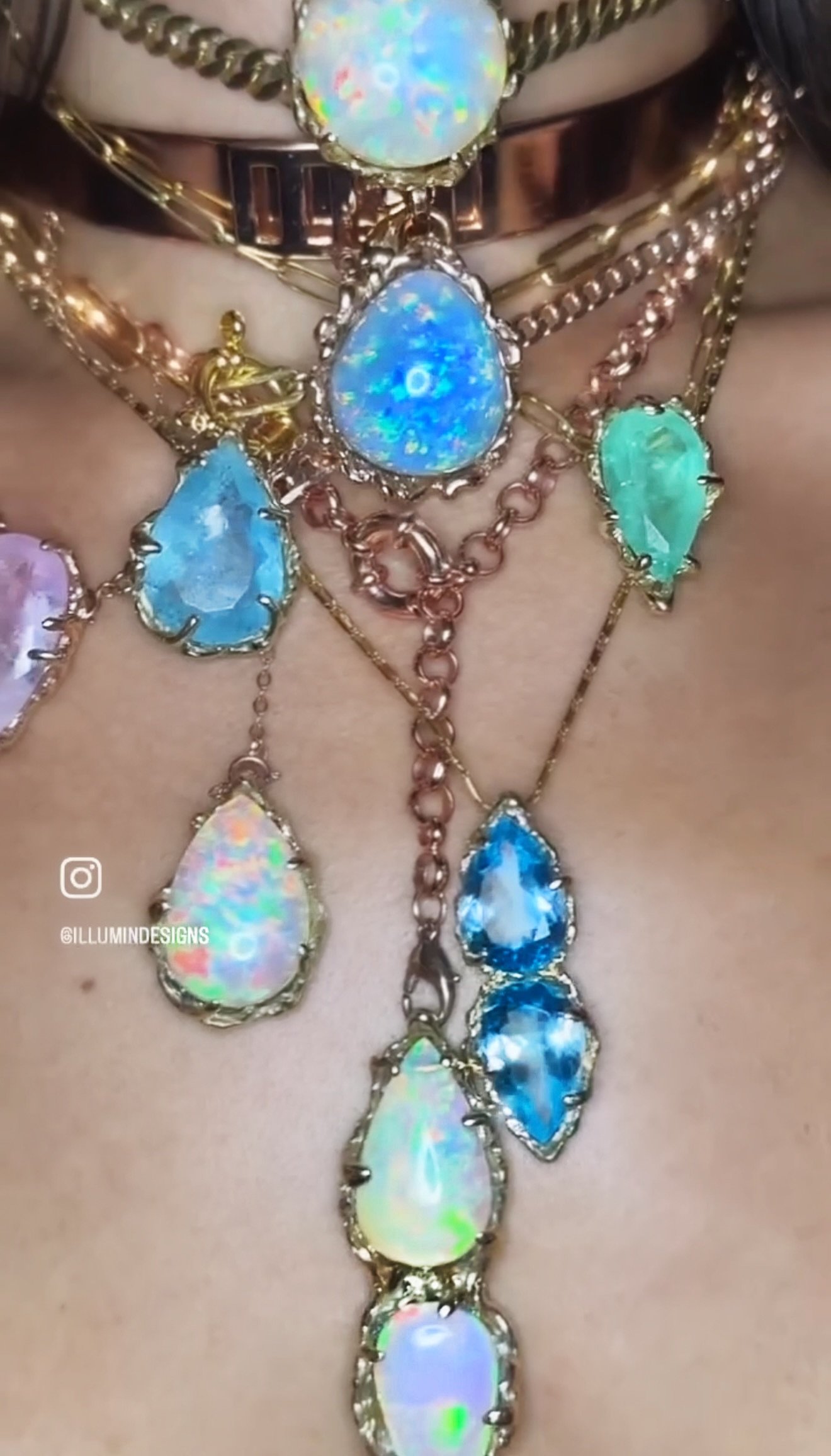 Multiple layered necklaces with large, colorful opal and blue gemstones, adorned with gold chains, worn around a person's neck.