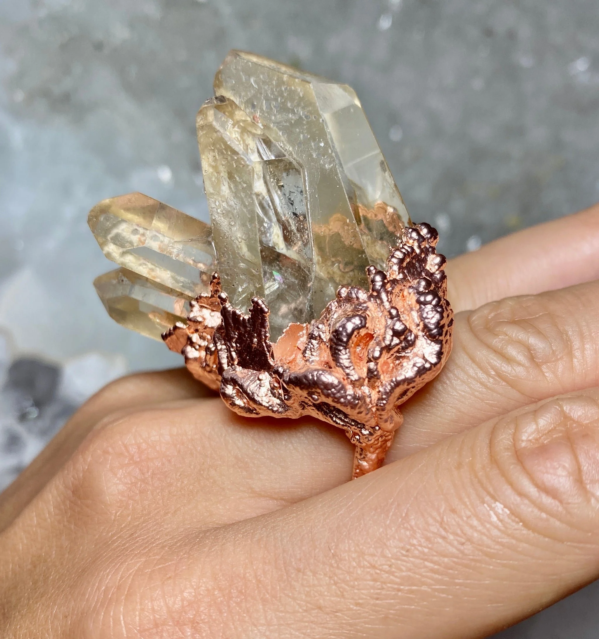 A hand wearing a ring with a large, clear quartz crystal cluster set in a textured copper band.