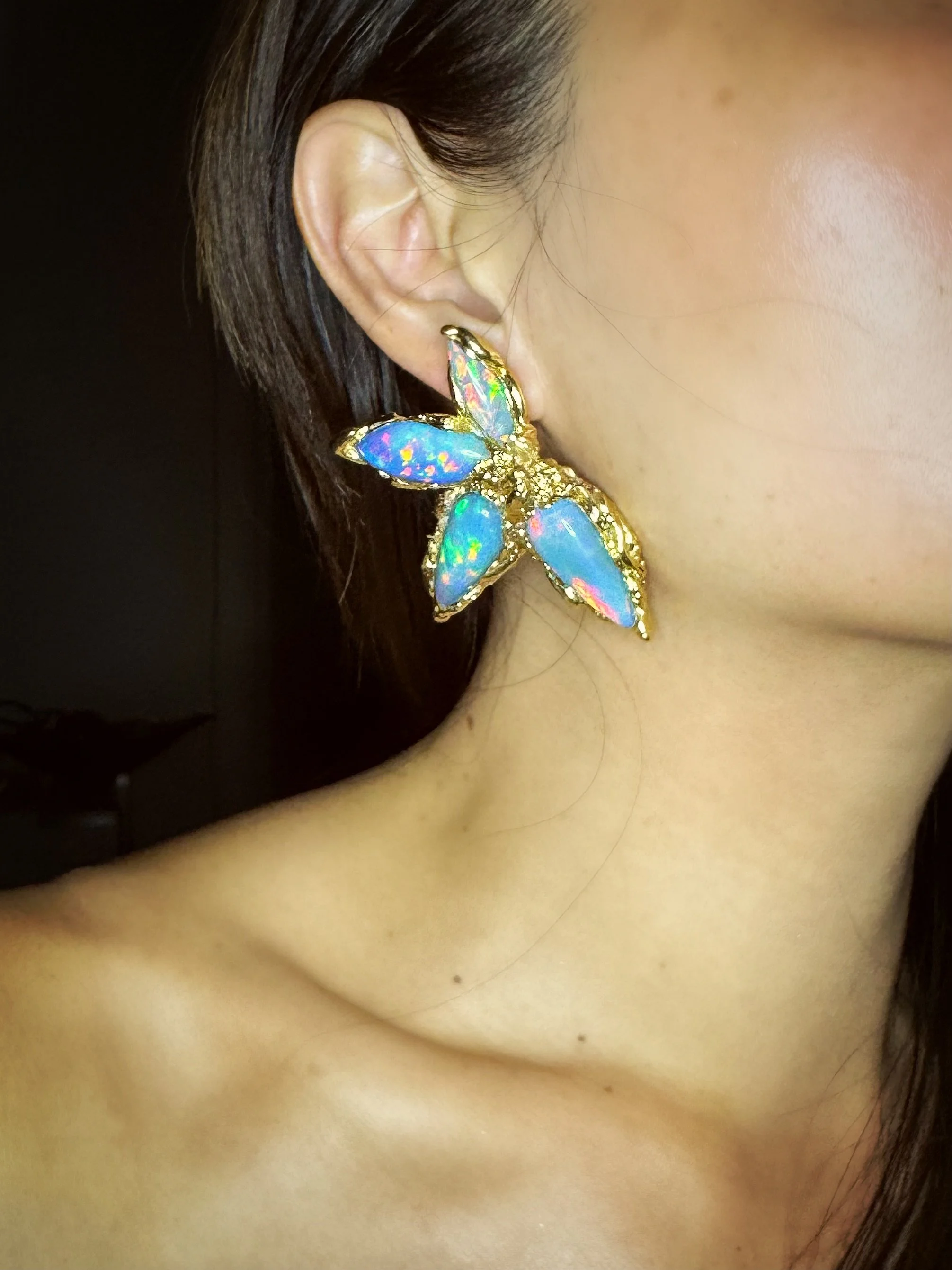 Close-up of a woman's ear with a large, colorful butterfly-shaped earring featuring blue and iridescent stones in gold settings.