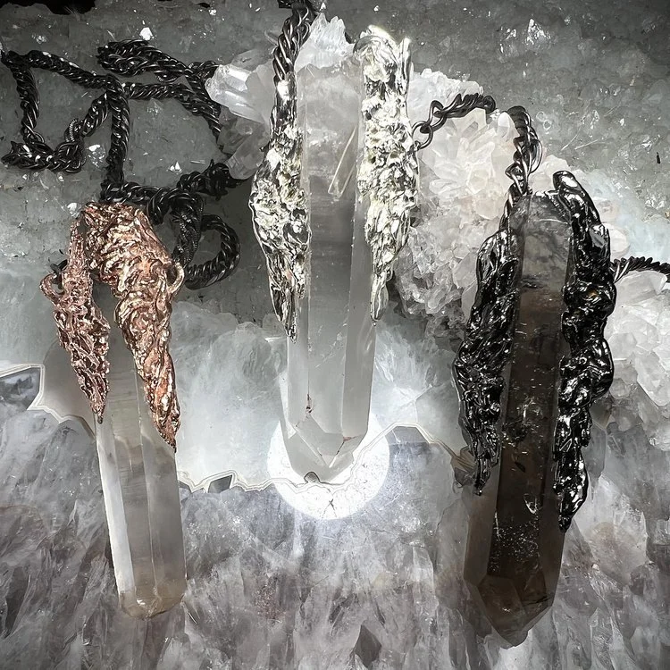 Three crystal pendant necklaces with metal caps, placed on a bed of clear quartz crystals.