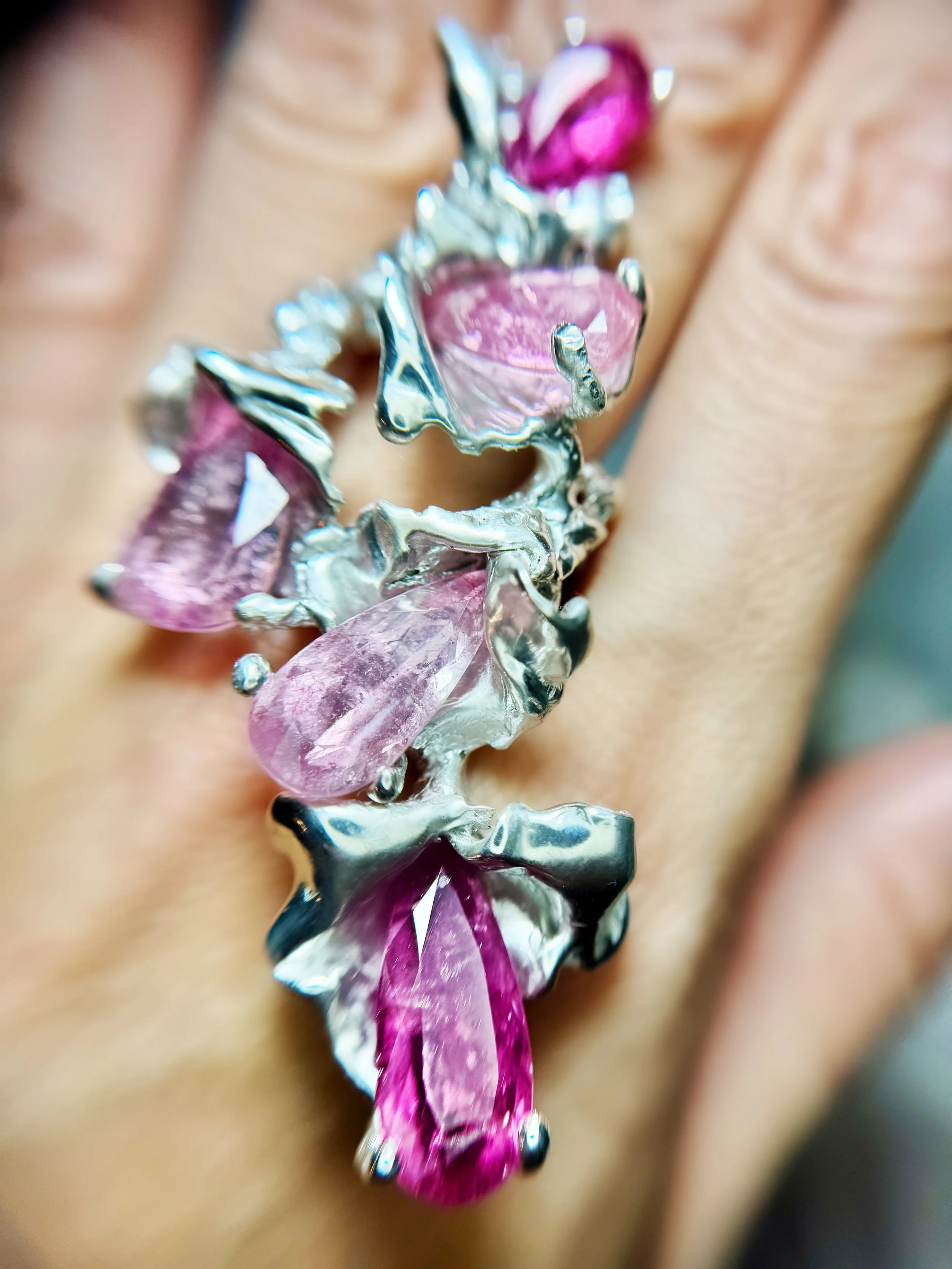 Close-up of a silver ring with large pink and purple gemstones on a person's finger.