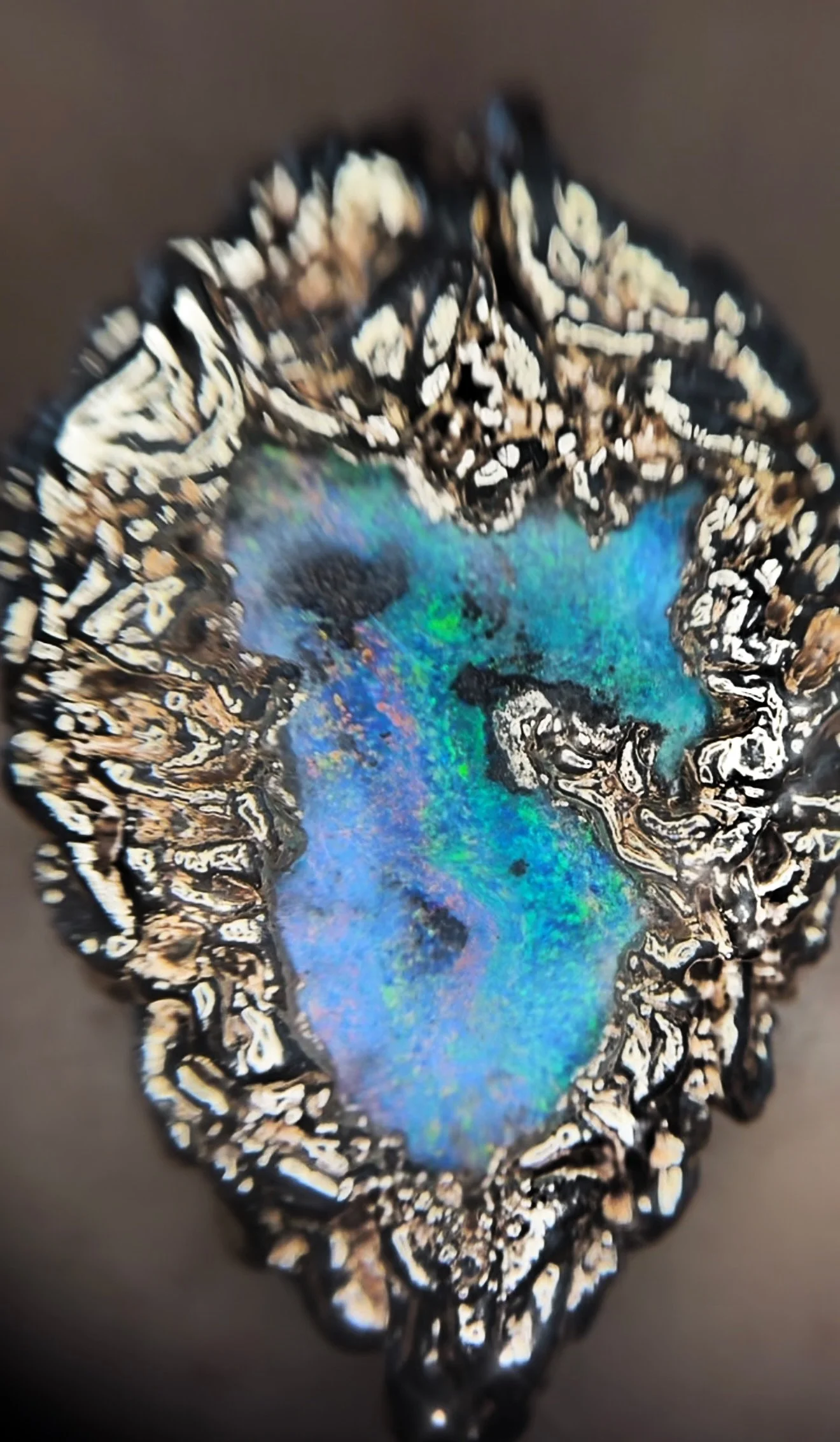 Close-up of an ornate, irregularly shaped ring with a multicolored, textured gemstone set in a silver and black patterned band.