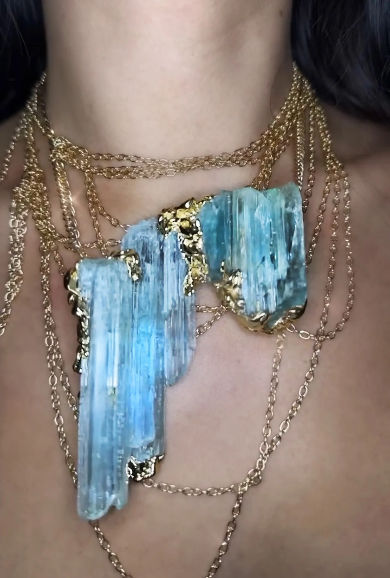 Close-up of a woman wearing multiple layered gold chains with a large pendant made of blue-green stone.