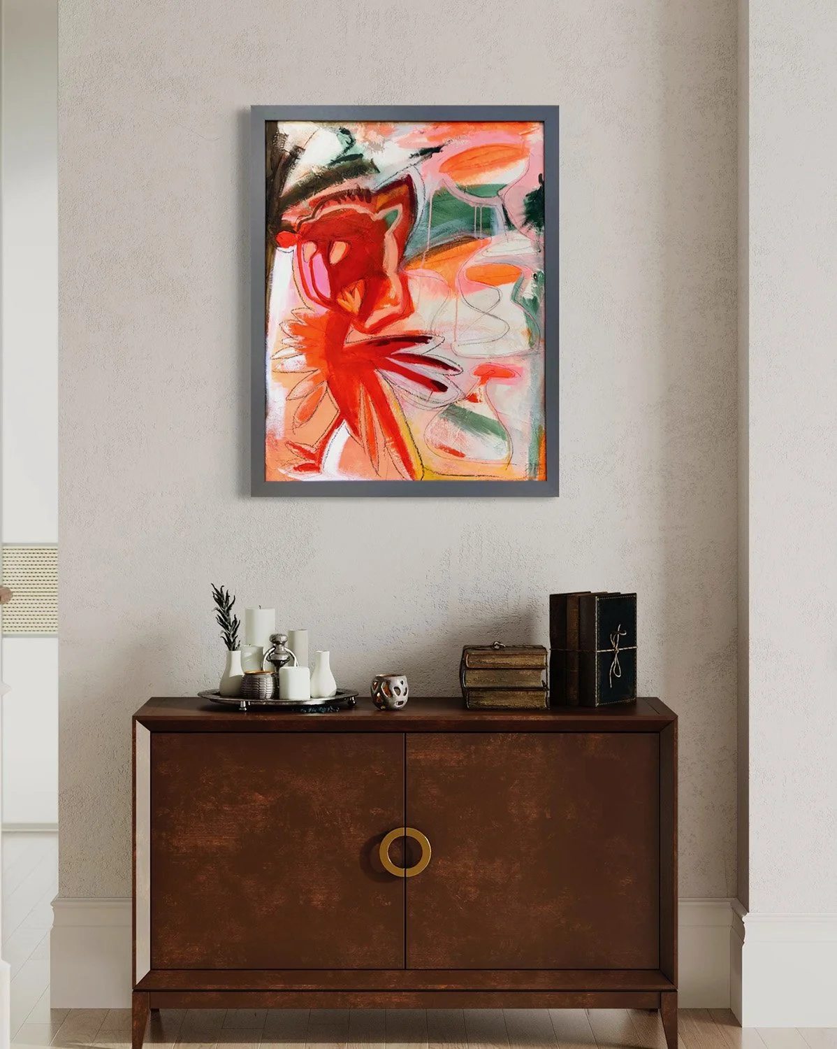An abstract colorful painting with reds, oranges, greens, and pinks hangs on a light-colored wall above a wooden cabinet decorated with various candles, vases, and books.