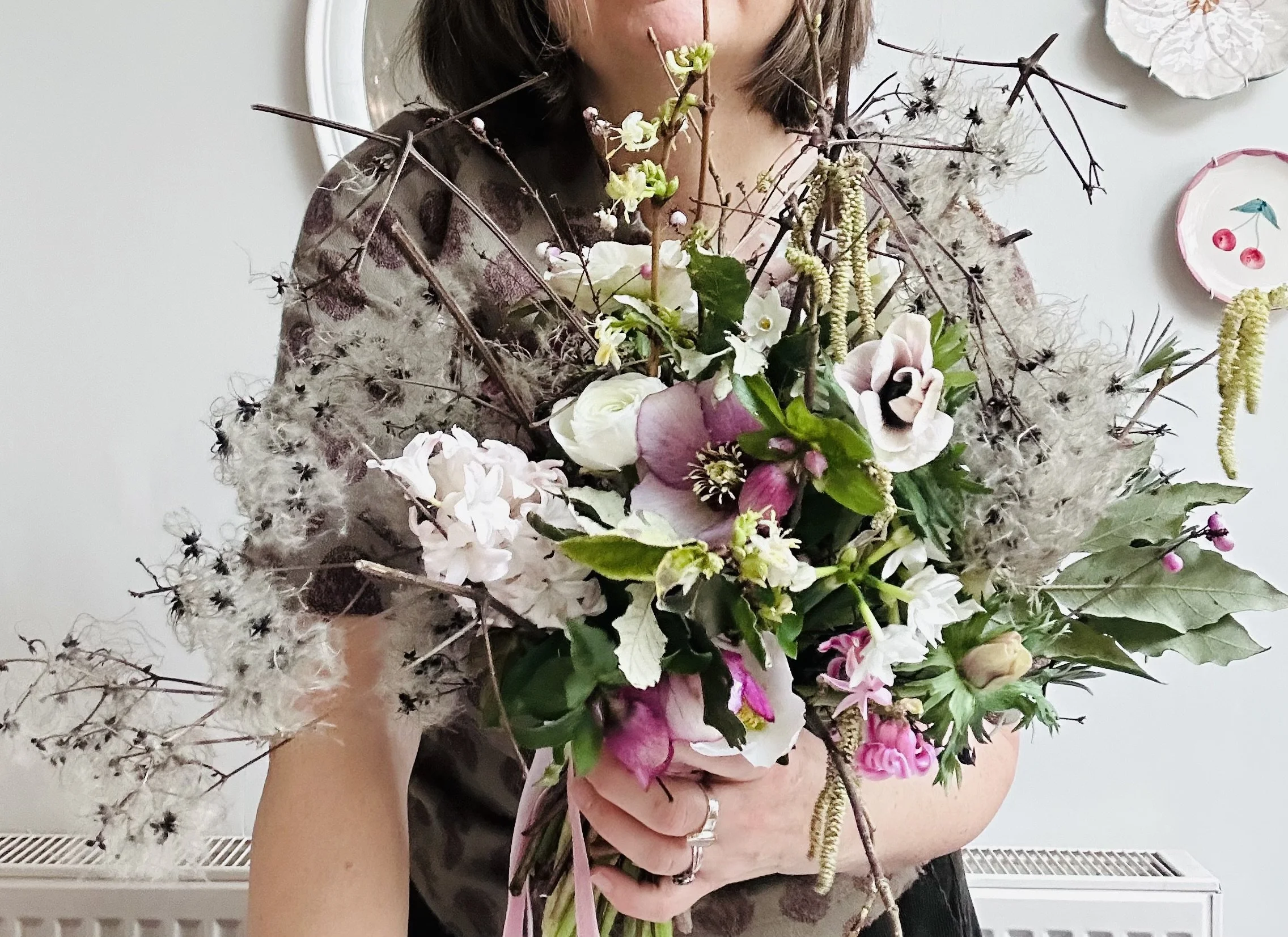 A woman holding a large bouquet of various flowers and branches.