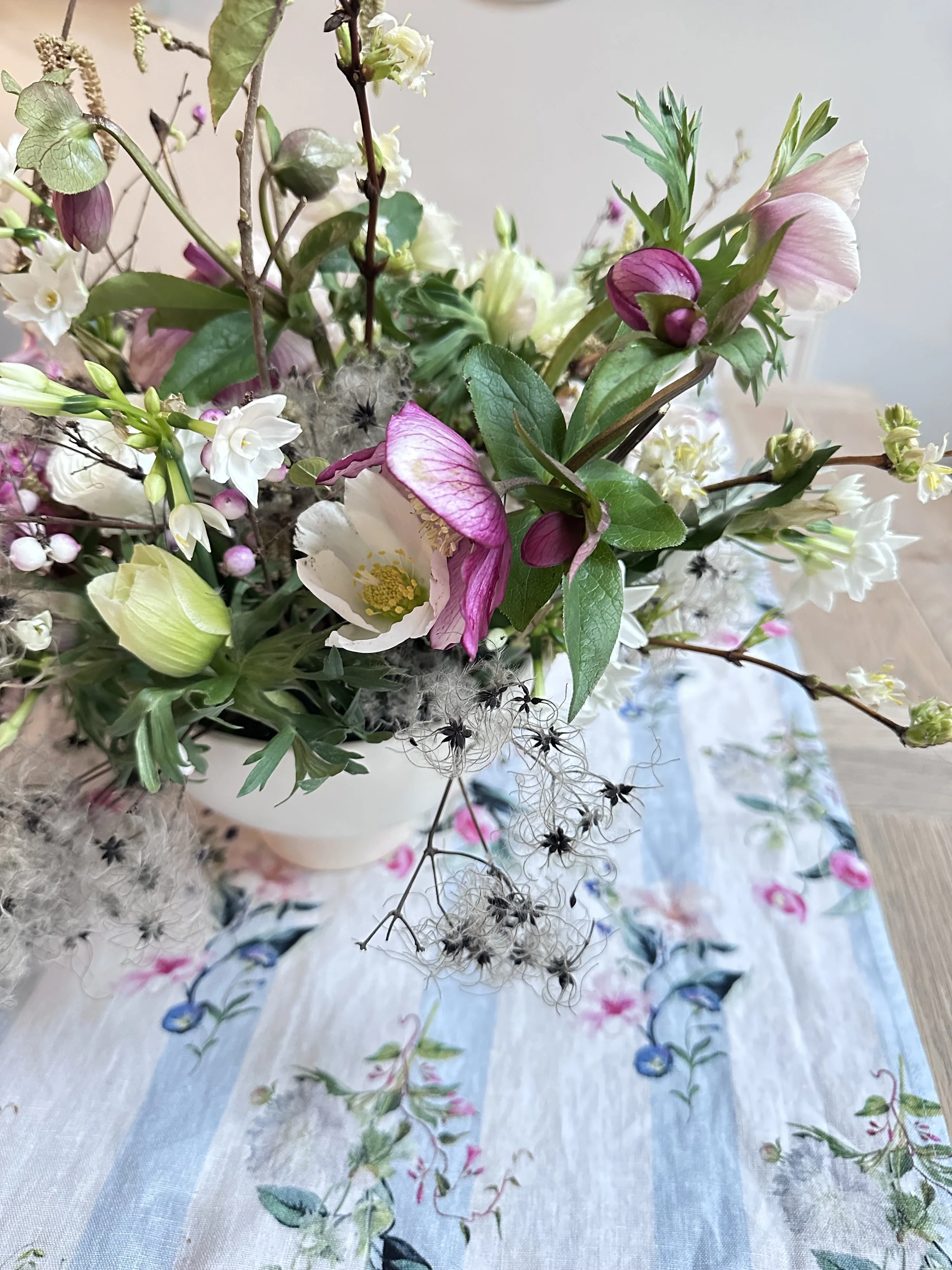 A close-up of a bouquet of mixed flowers and greenery arranged on a table with a floral tablecloth.