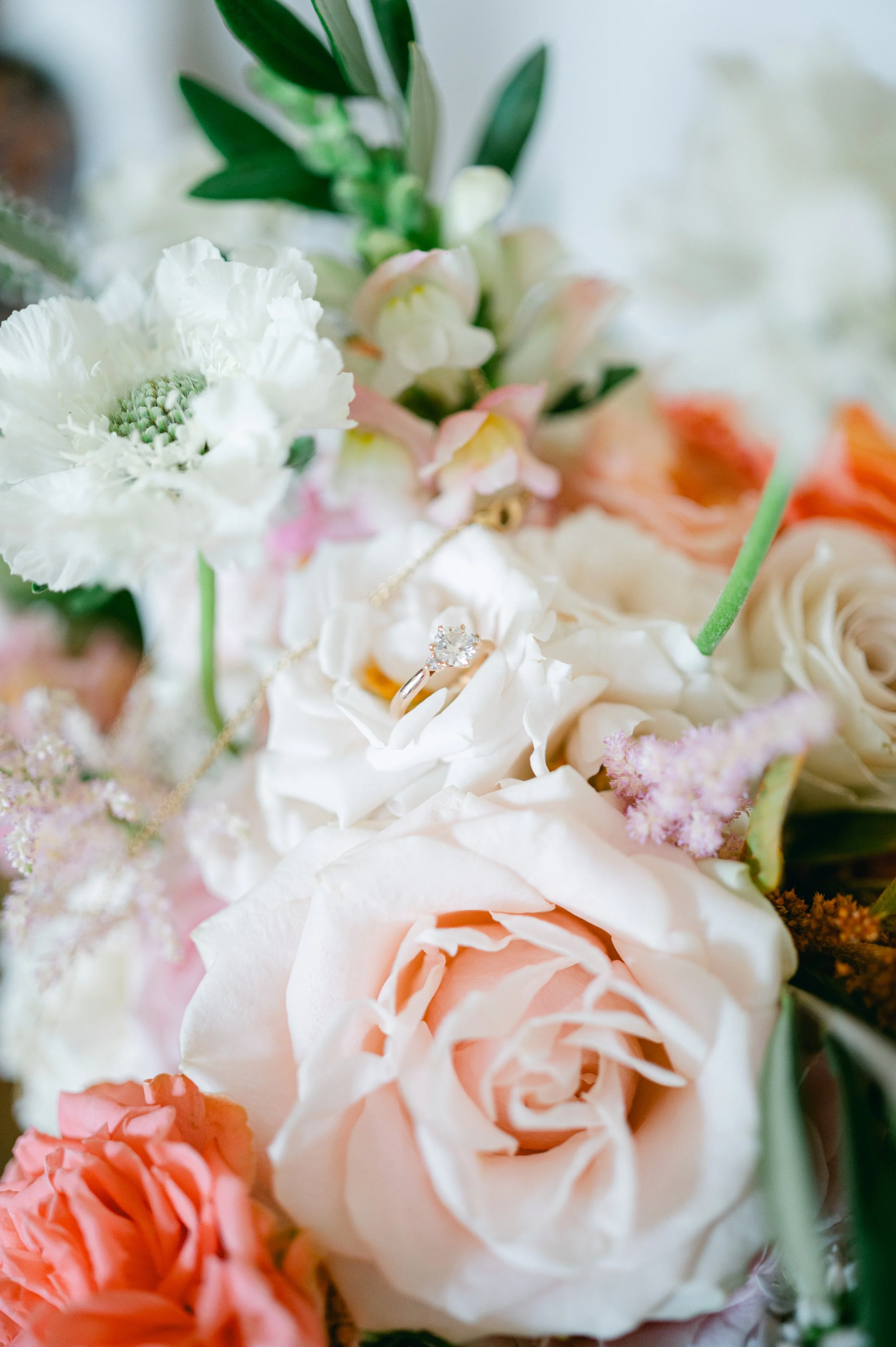 A close-up of a bouquet of various flowers with a diamond engagement ring resting on a white flower.