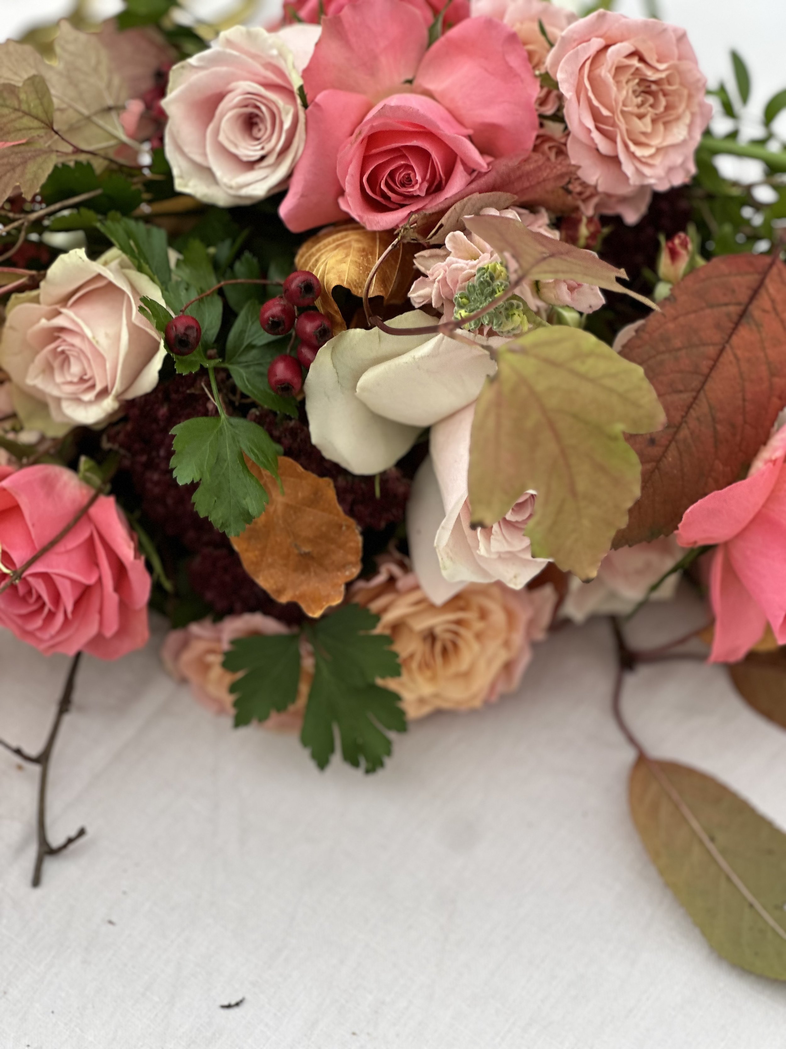 Close-up of an autumn bouquet with pink and blush roses, beech leaves, snowberries, and hawthorn by Foxgloves & Roses