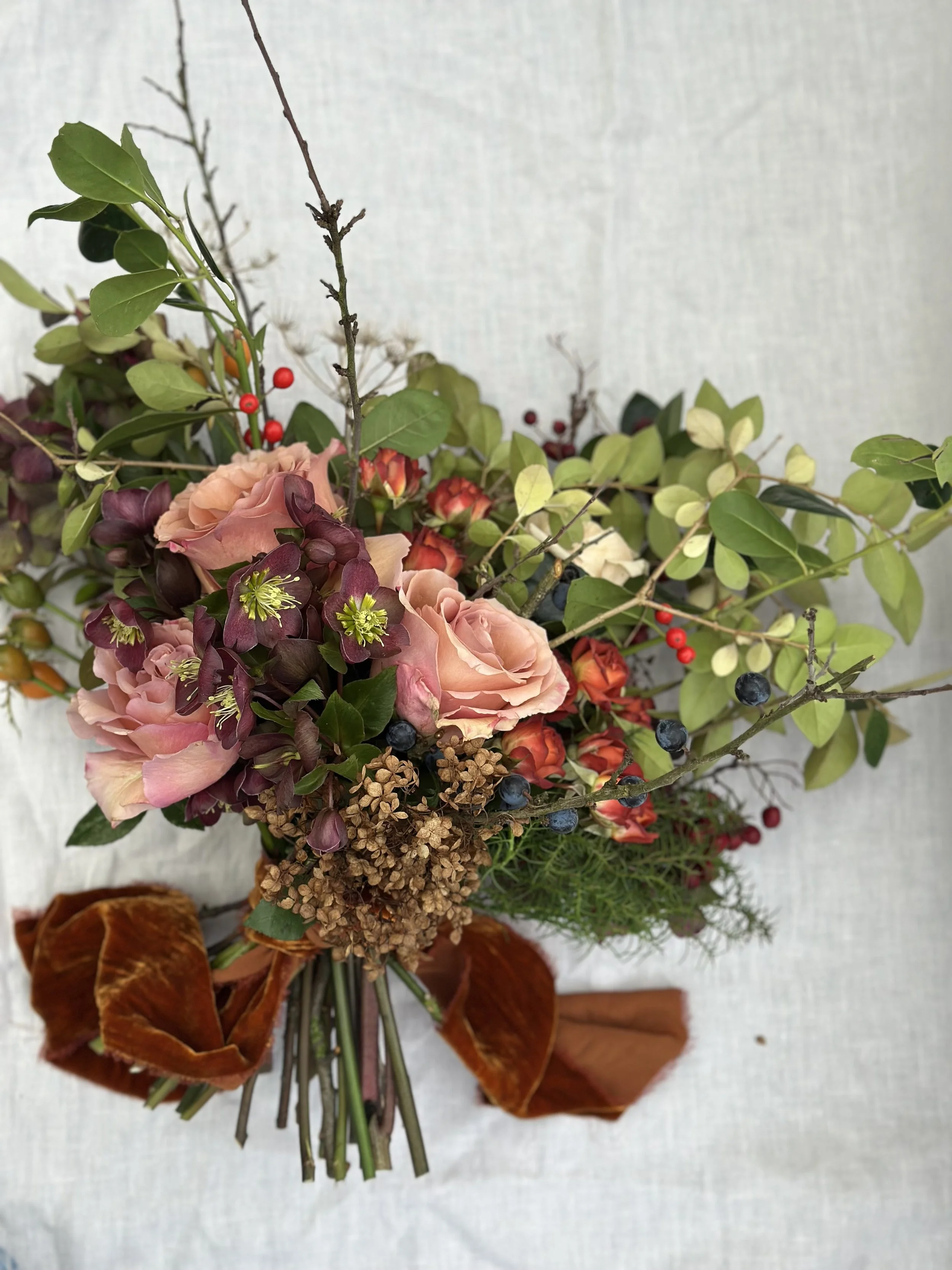 A mixed bouquet of flowers, leaves, and berries arranged on a white surface.