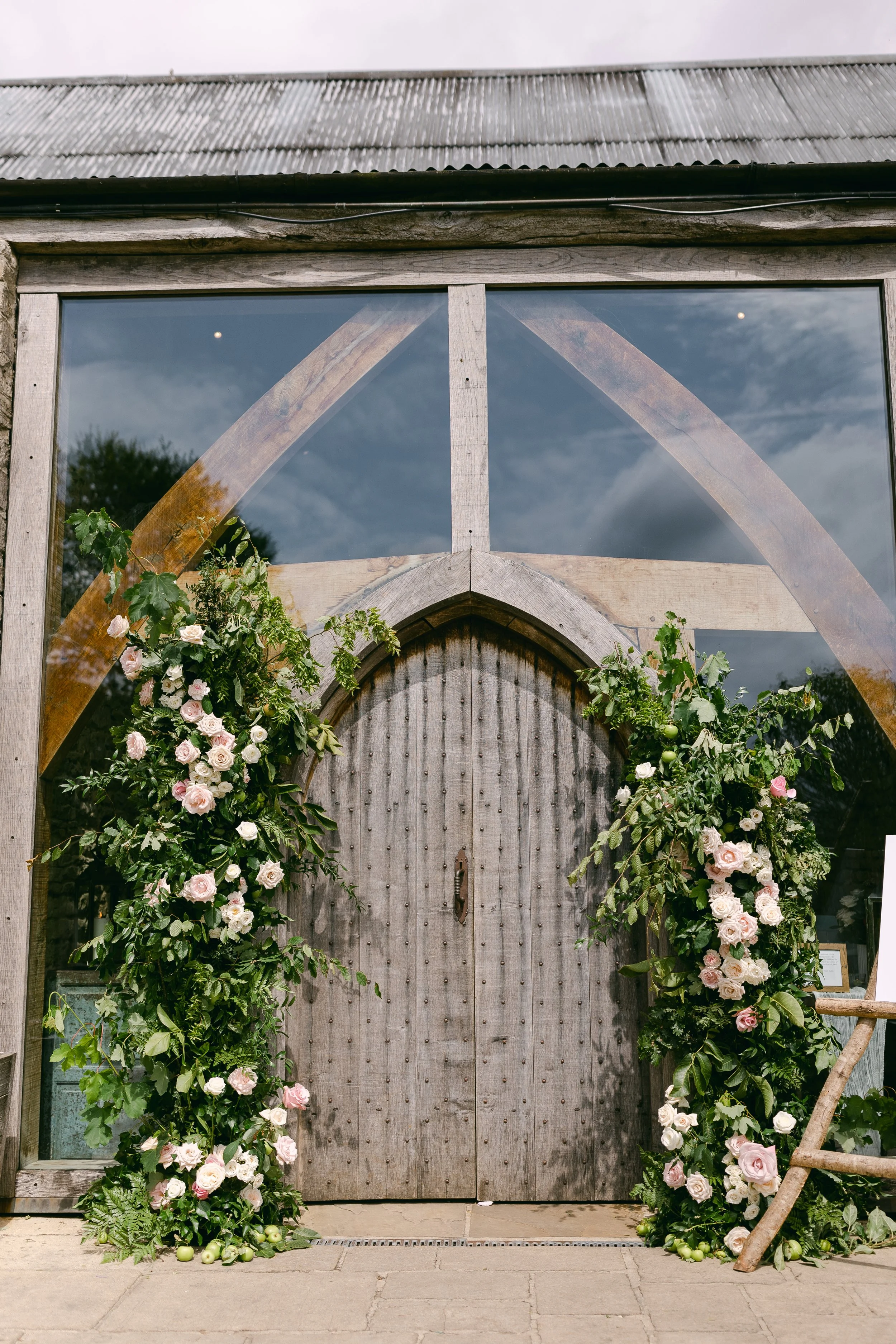 Romantic blush and pale green summer flower pillars framing an outdoor ceremony entrance.