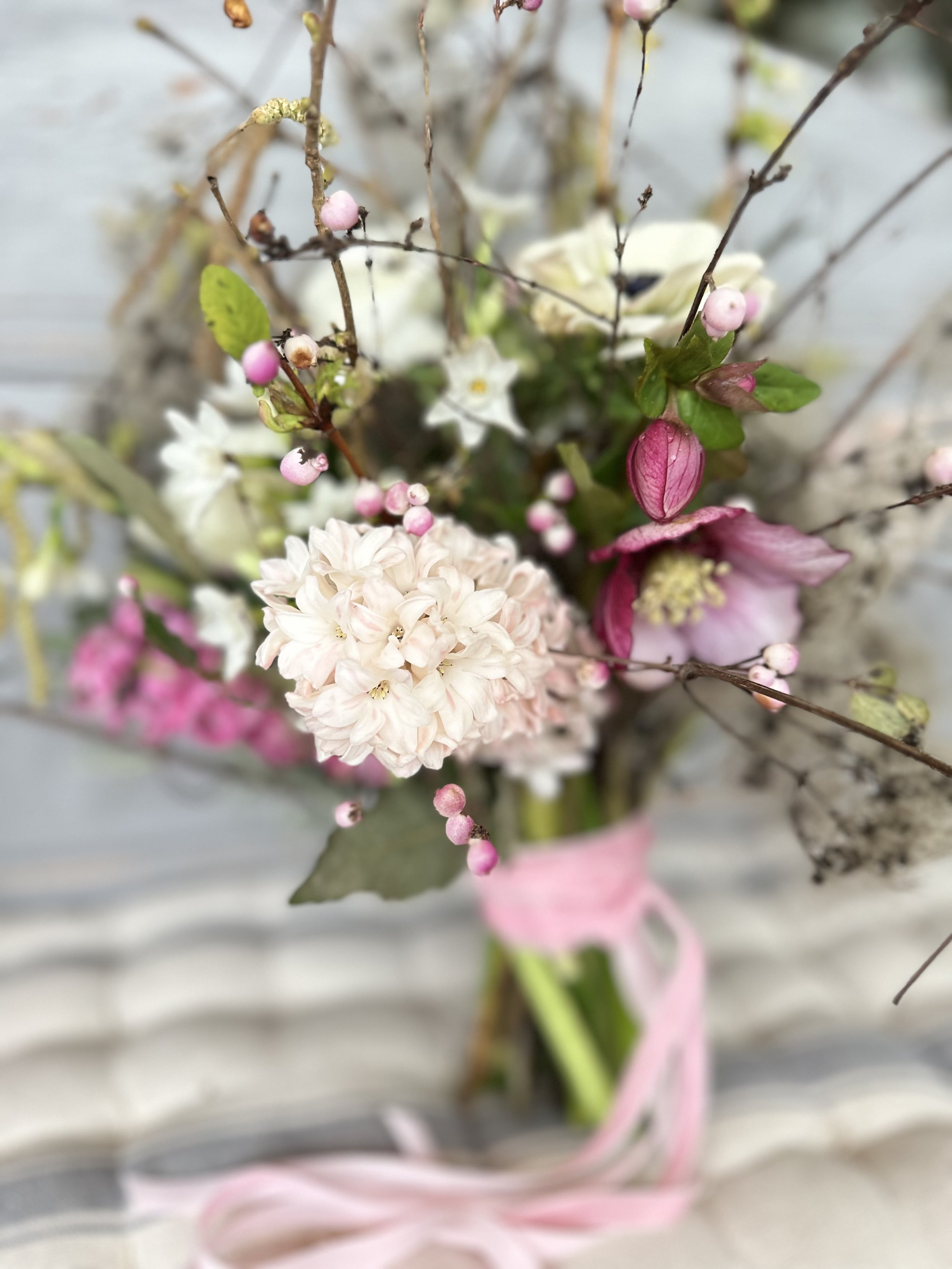A close-up of a bouquet with pink and white flowers, small pink buds, and green leaves, tied with a pink ribbon.
