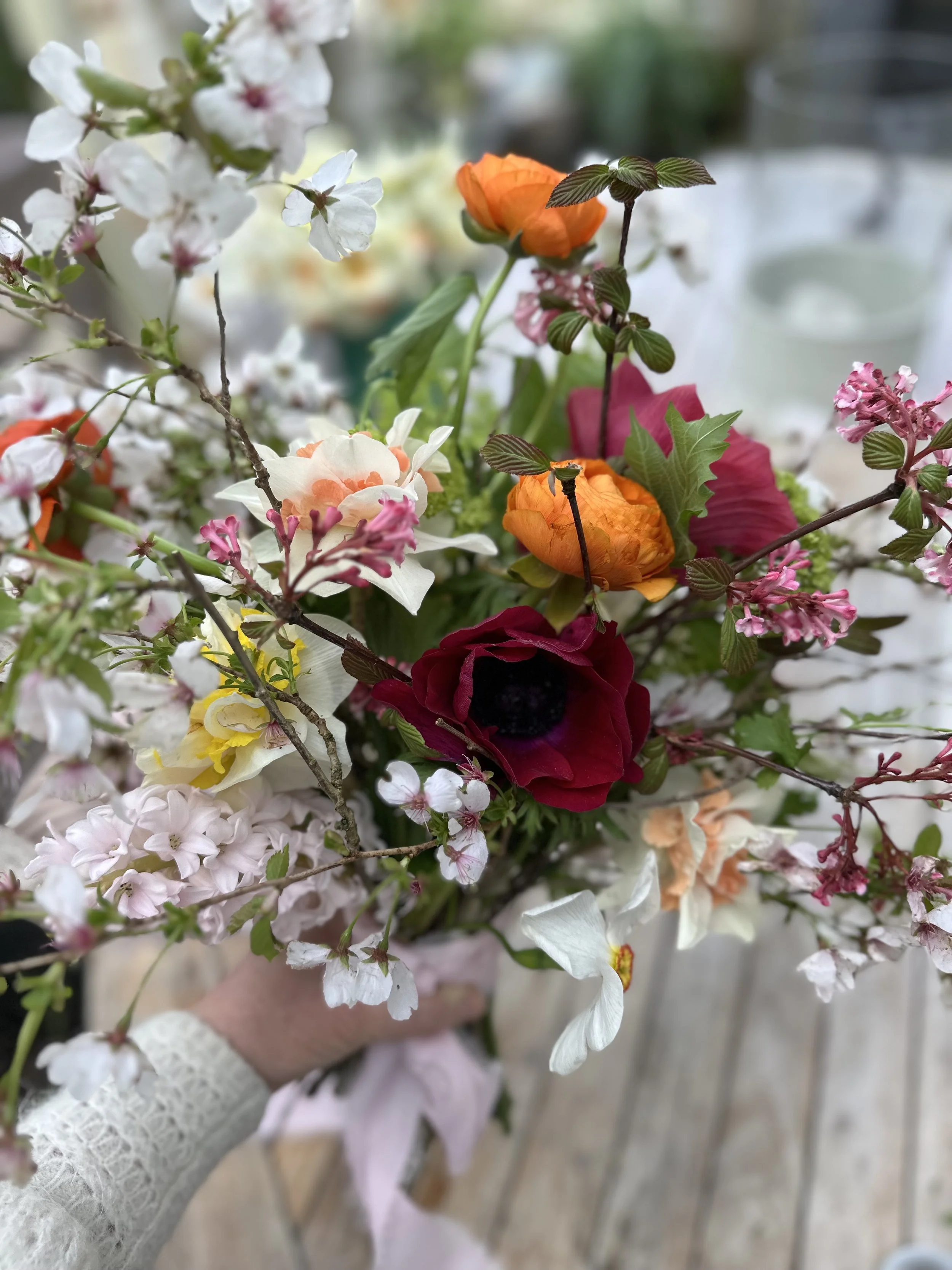 Close-up of a floral bouquet with white, pink, orange, red, and yellow flowers, and green leaves and stems.