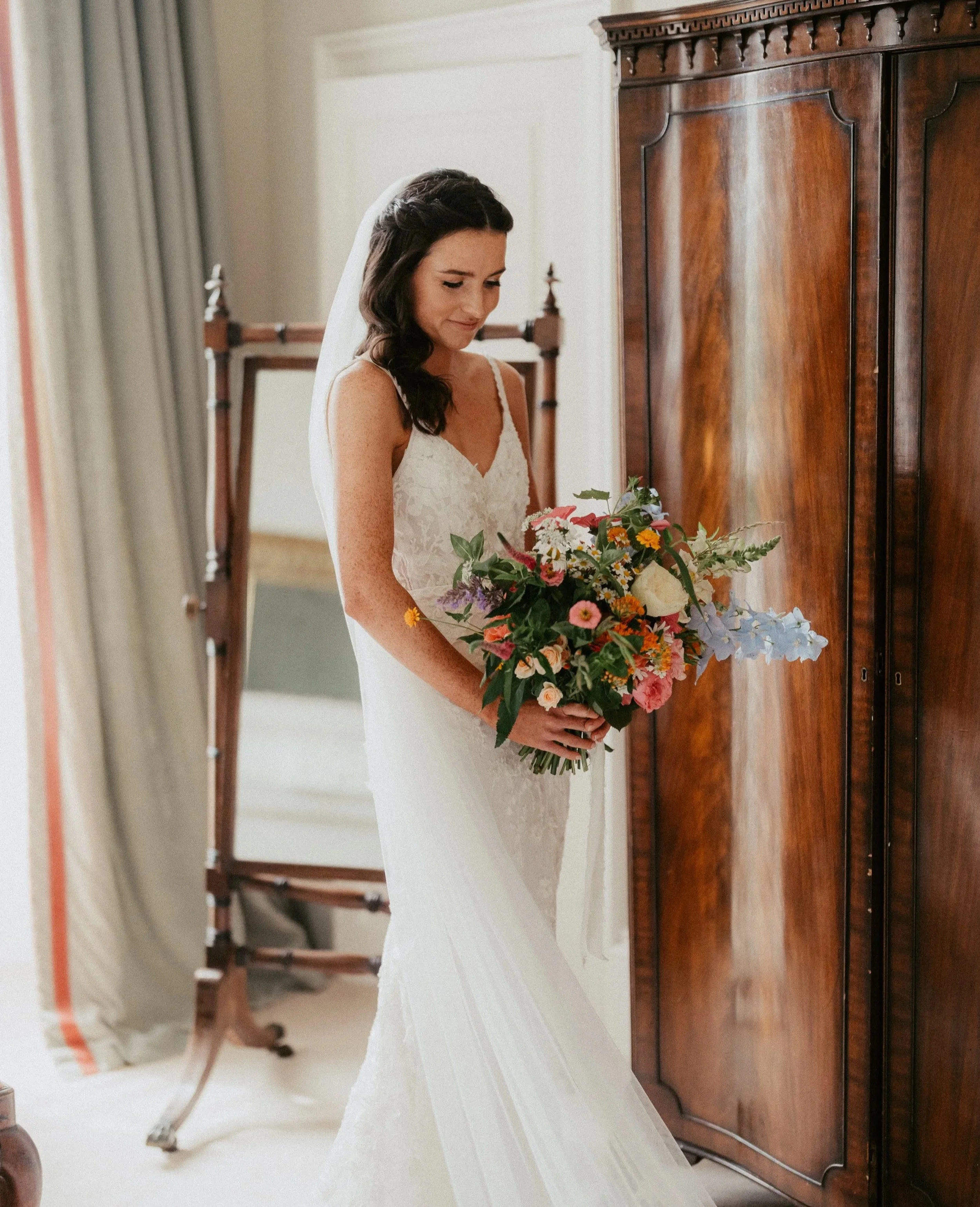 Bride holding a vibrant sunset-toned summer bouquet with coral, apricot, and wildflower textures.