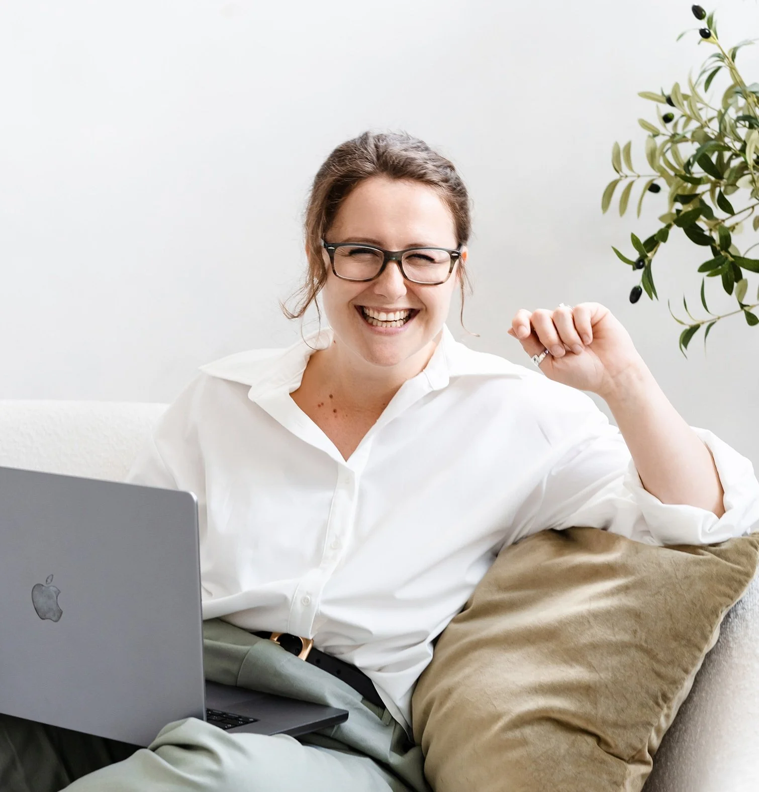 Sophie the founder and Squarespace SEO specialist at Studio Soph is wearing a white shirt, sat on a cream sofa with a laptop on her lap smiling at the camera