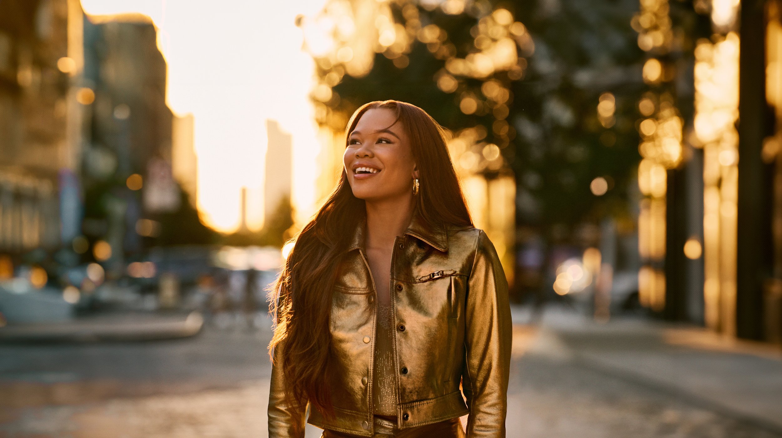 Storm Reid Coach Gold fragrance campaign, walking on NYC street at golden hour in gold leather jacket, photographed by Cass Bird casting and production by Boom Productions
