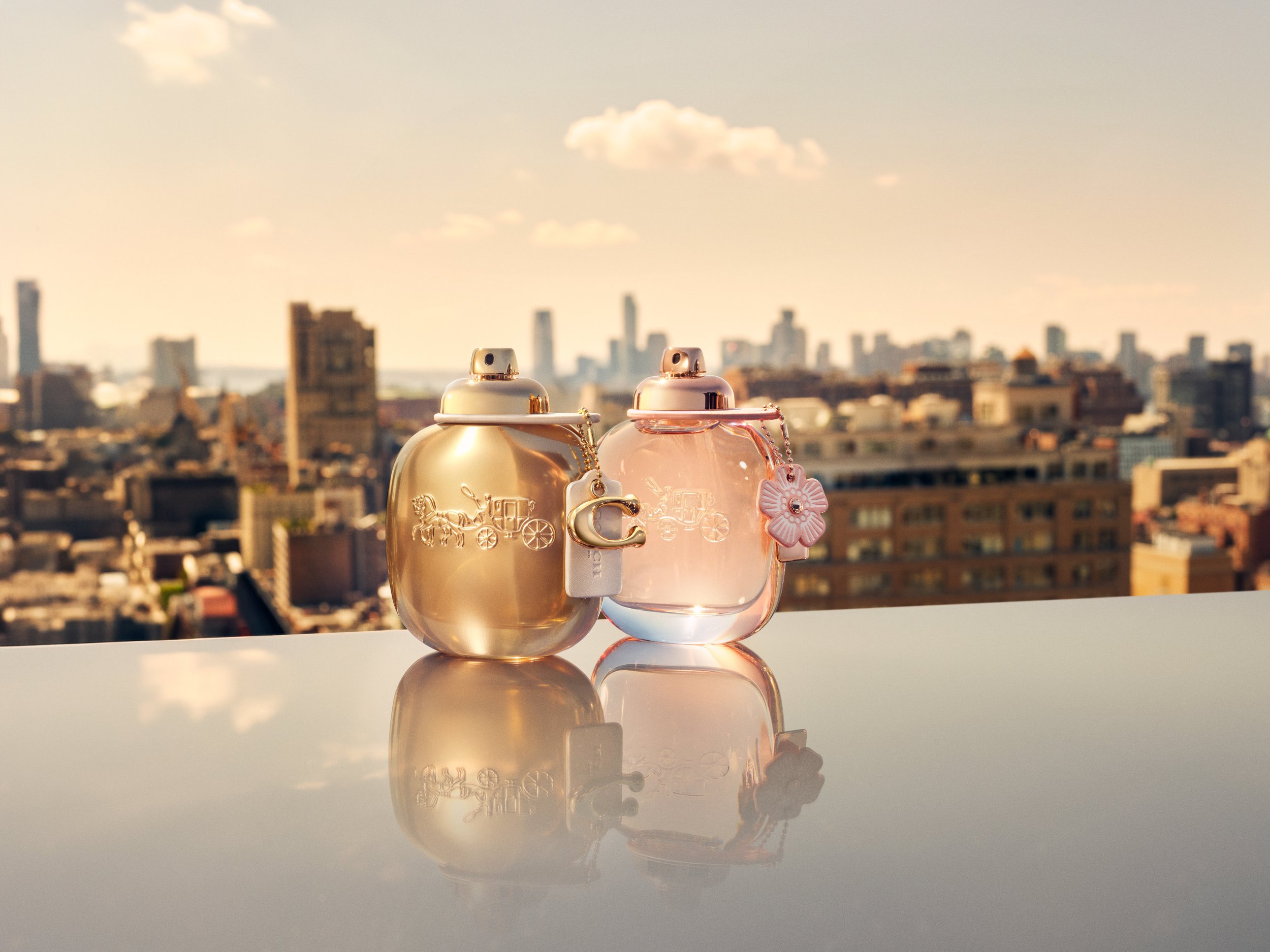 Coach Floral and Coach Gold eau de parfum bottles on reflective surface with NYC skyline, photographed by Cass Bird