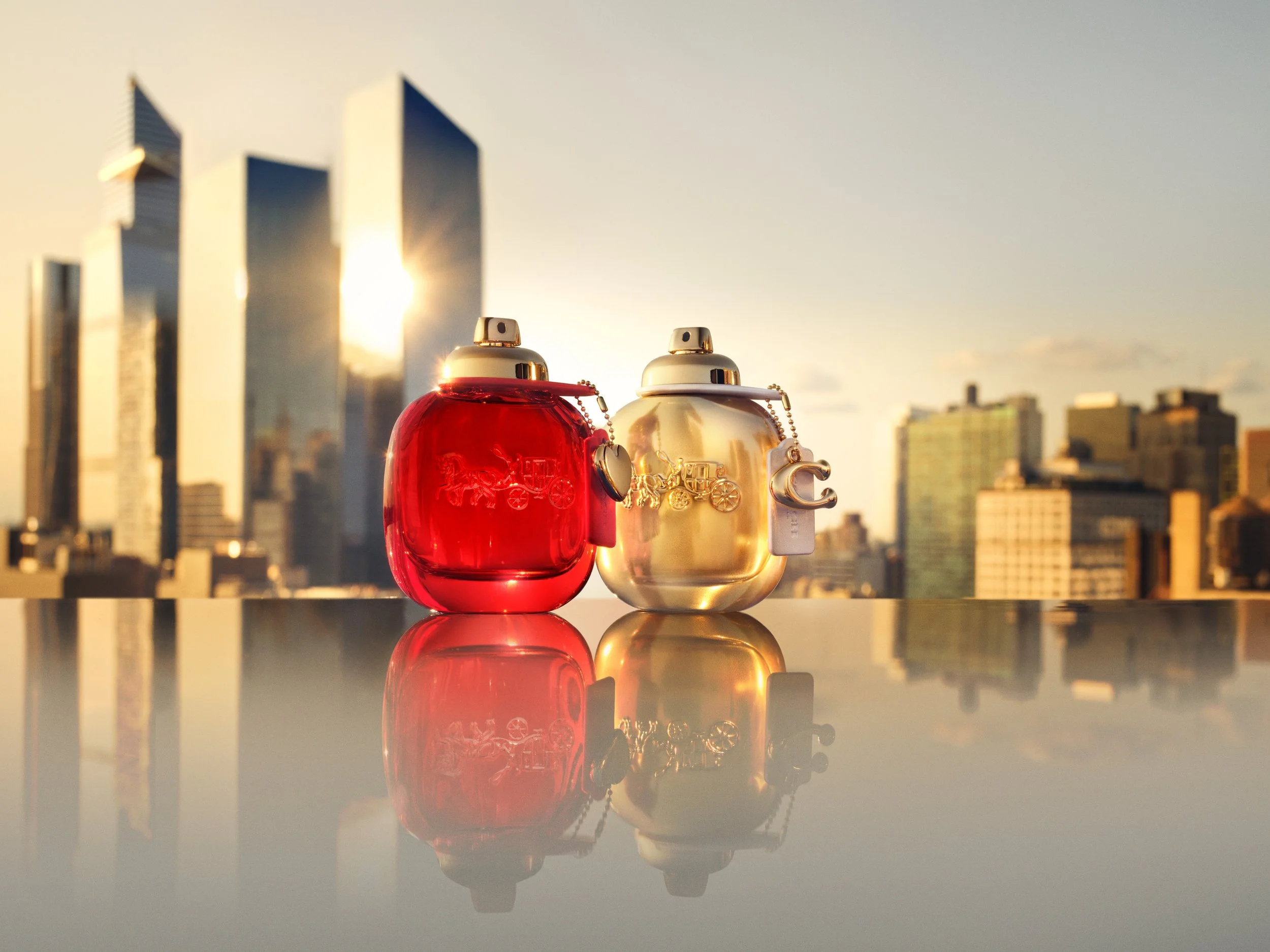 Coach Love and Coach Gold eau de parfum bottles on reflective surface with NYC skyline at sunset, photographed by Cass Bird
