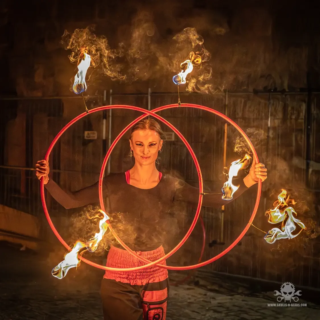 Elena Tinkloh smiling through two overlapping fire hoops — joy and flow arts in practice