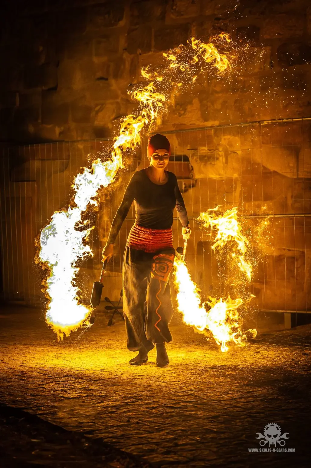 Elena Tinkloh walking toward the audience with lyco torches at ground level — fire performance