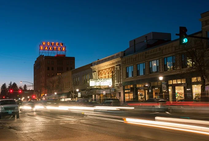 Nighttime city street with cars and light trails, buildings, hotel sign, and a traffic light