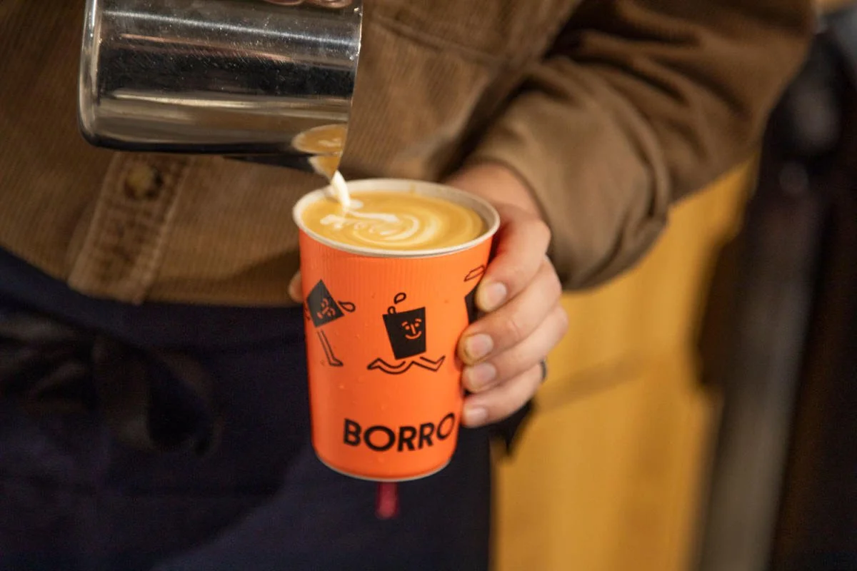 milk being poured into latte art in a borro cup orange cup.