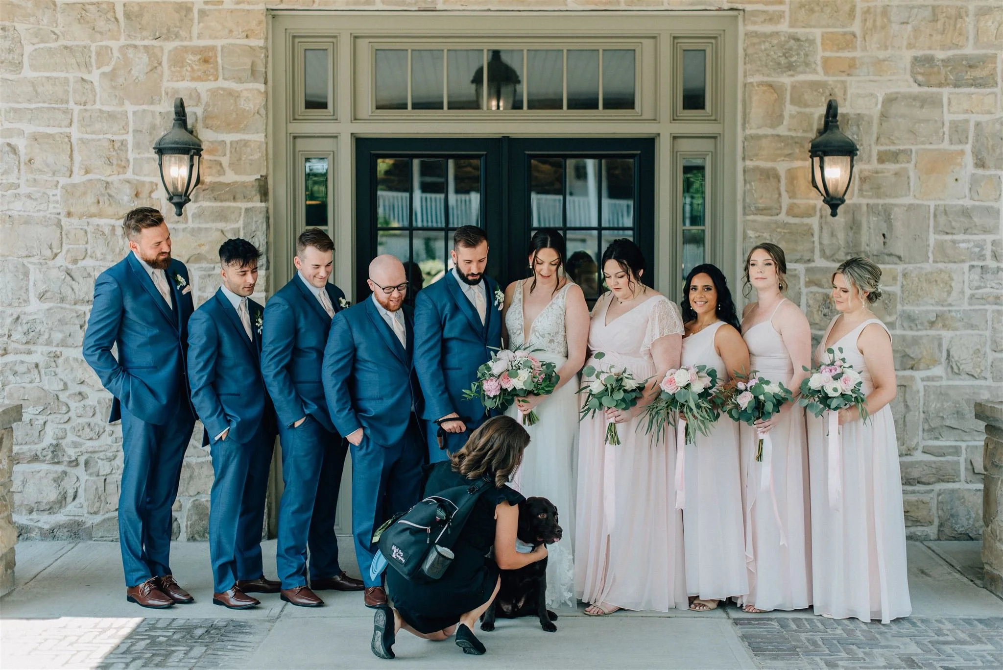 Black Dog Weddings wedding dog attendant Ash straightens labrador Archie's bandana for wedding photography with the wedding party in Ancaster Ontario