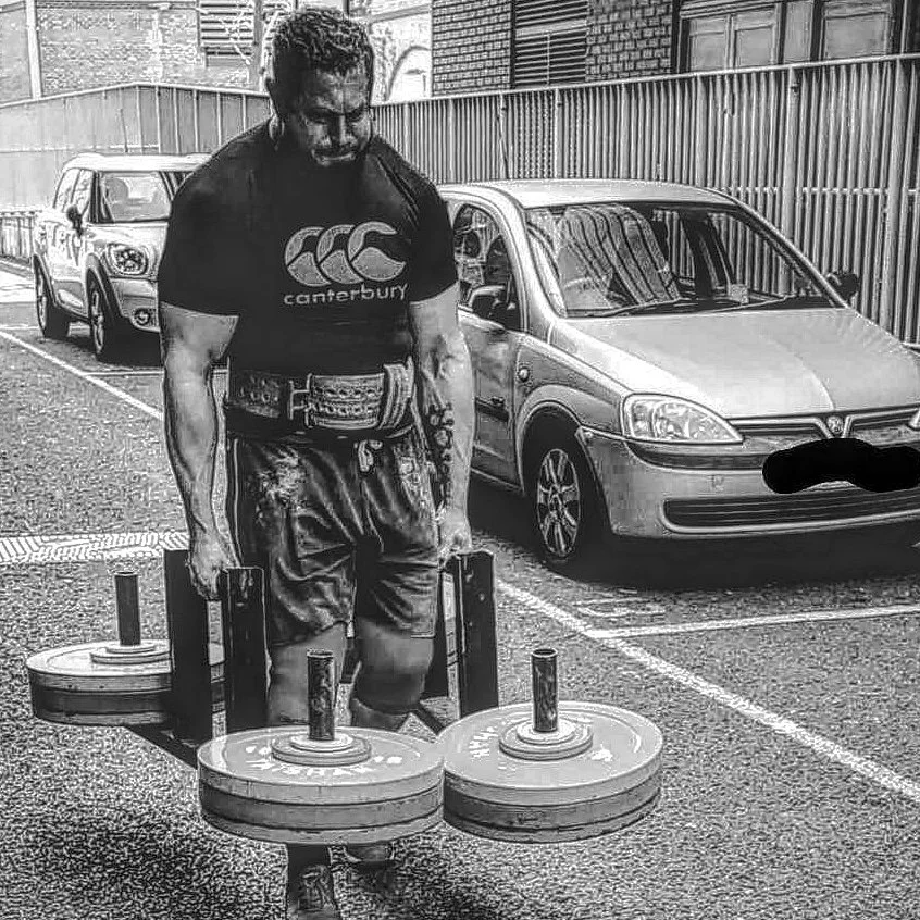 A man is carrying two heavy farmers walk handles in the street outside a gym
