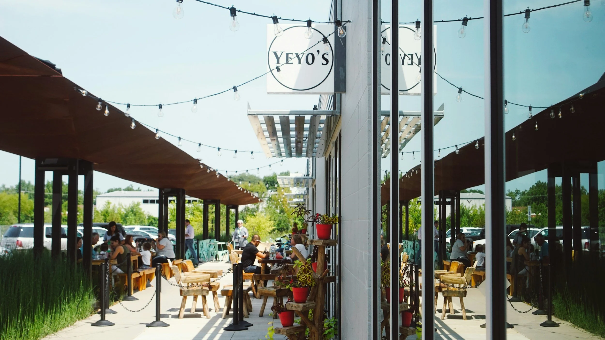 Outdoor patio of a café named YEYO'S with string lights overhead, people dining at tables, and parking visible in the background.