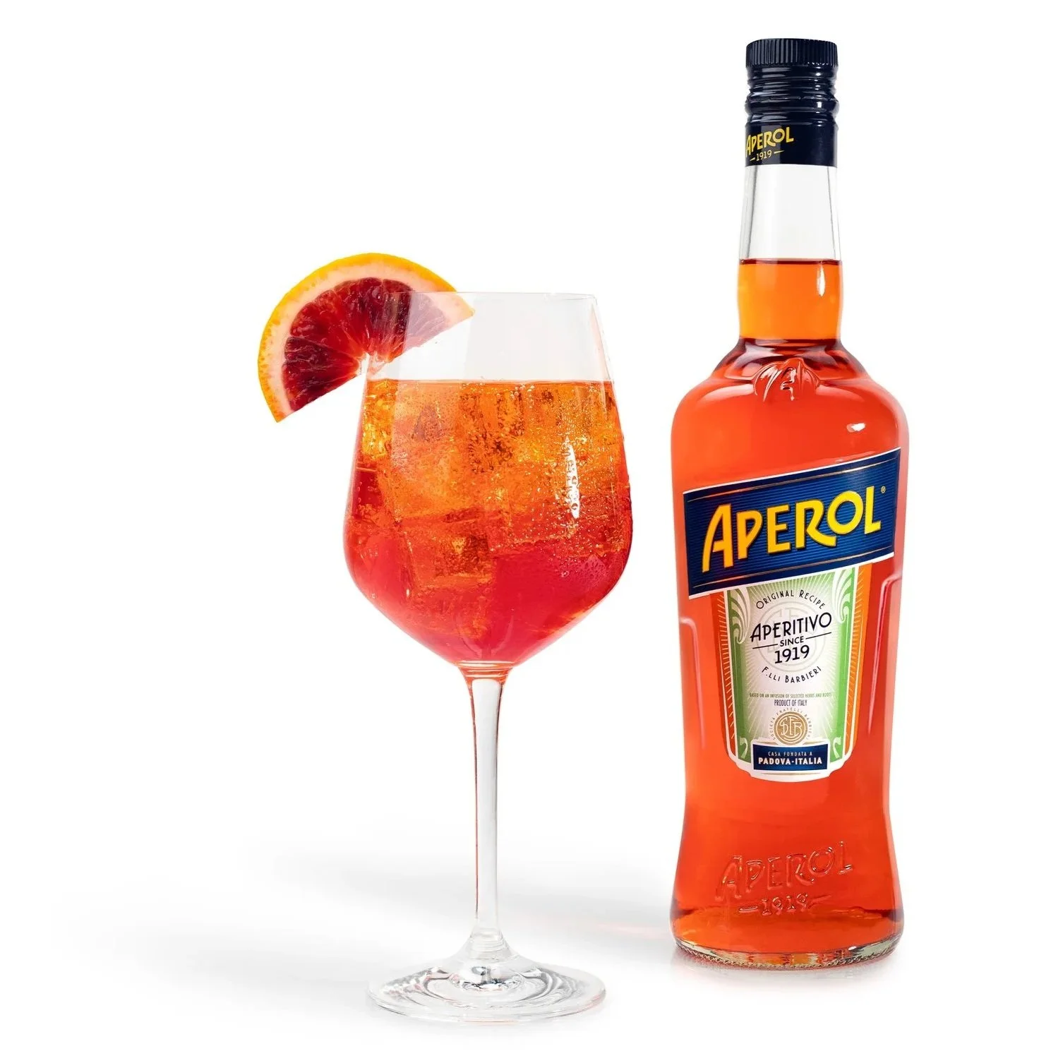 A glass of Aperol spritz garnished with a slice of blood orange, alongside a bottle of Aperol. The drink is orange with ice cubes, set against a white background.