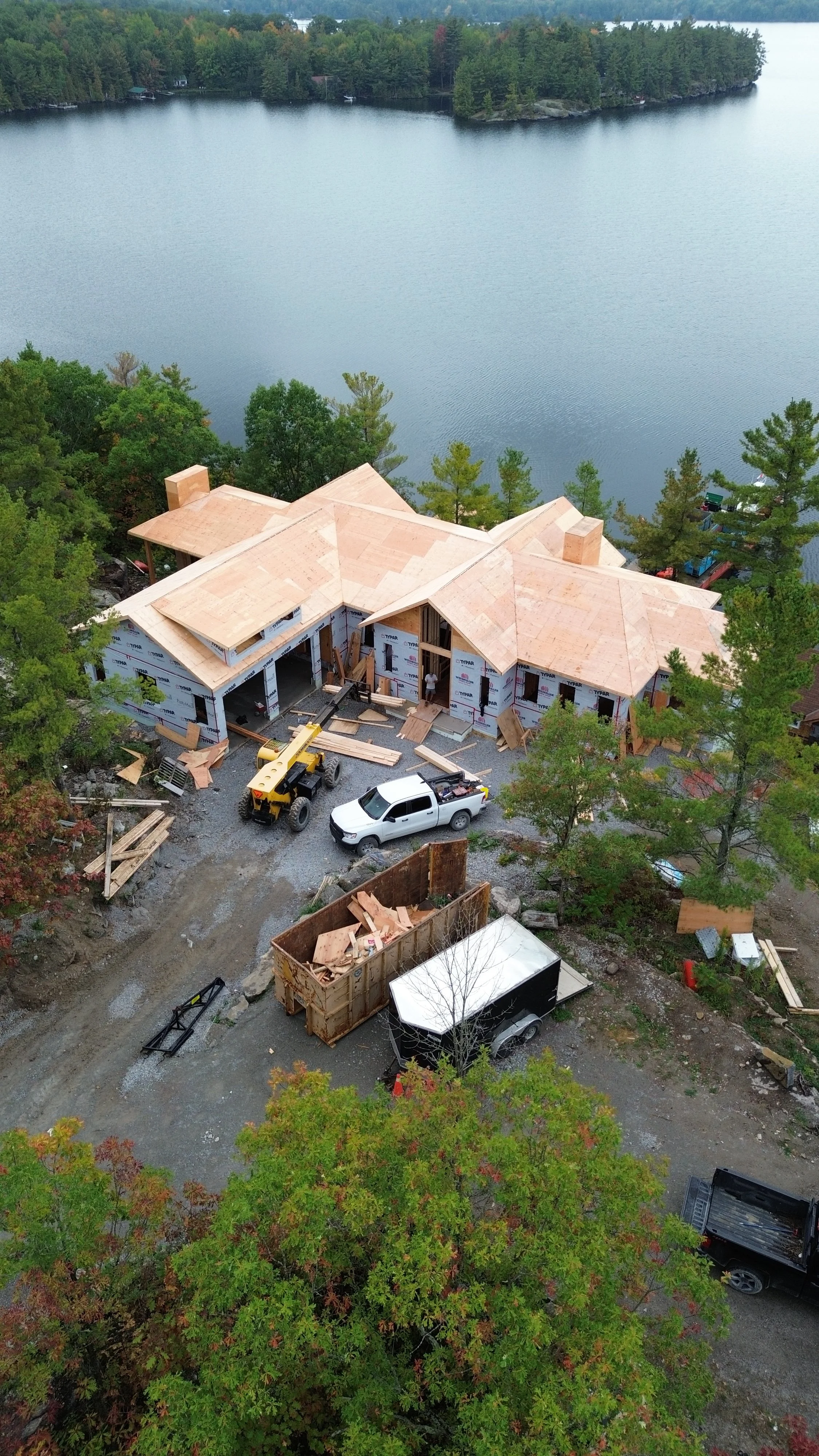 A house under construction near a lake, with construction vehicles and materials around.
