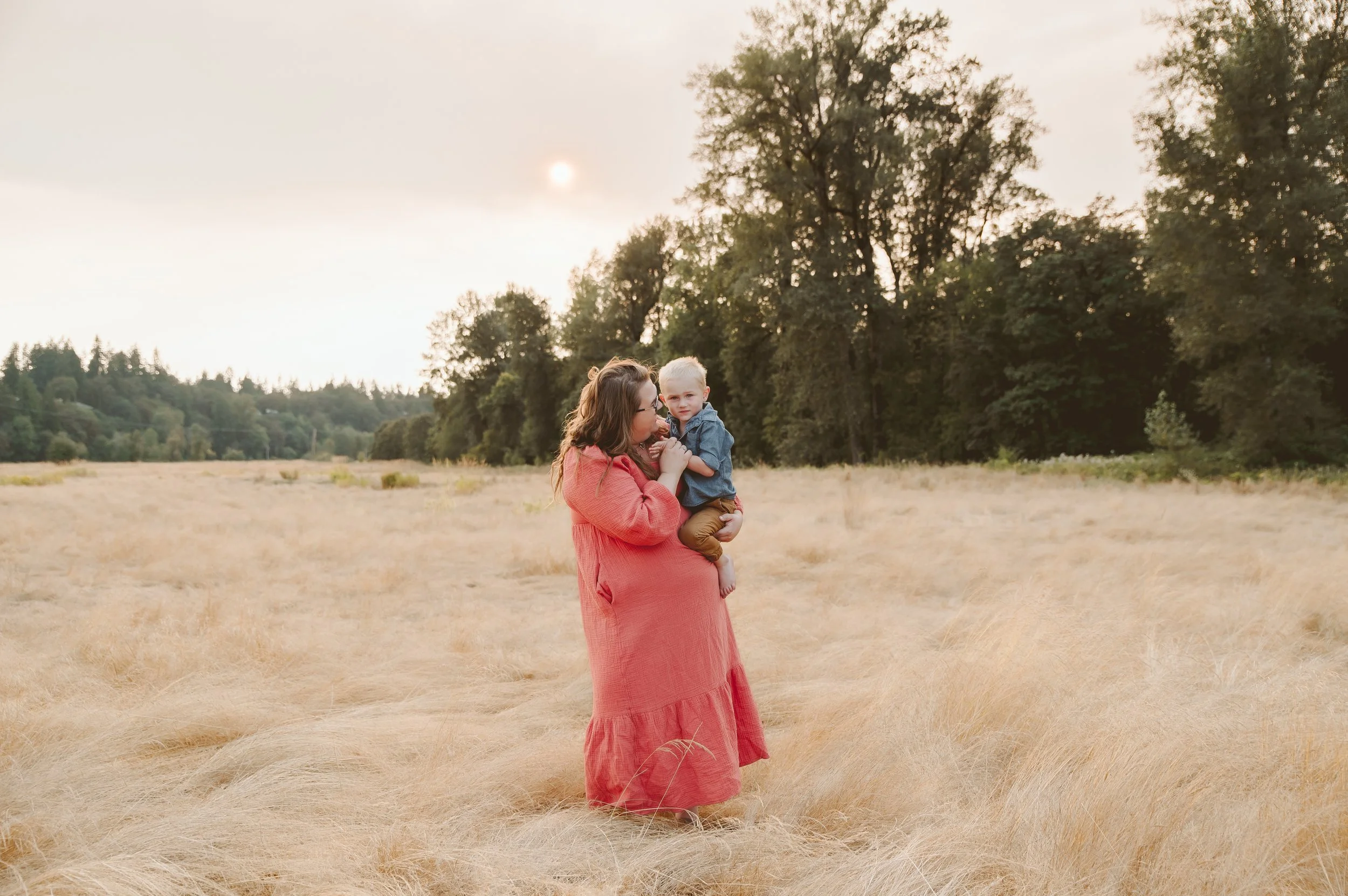 Motherhood portrait of a woman holding her child in a golden field during sunset, captured by a Vancouver Washington family photographer.
