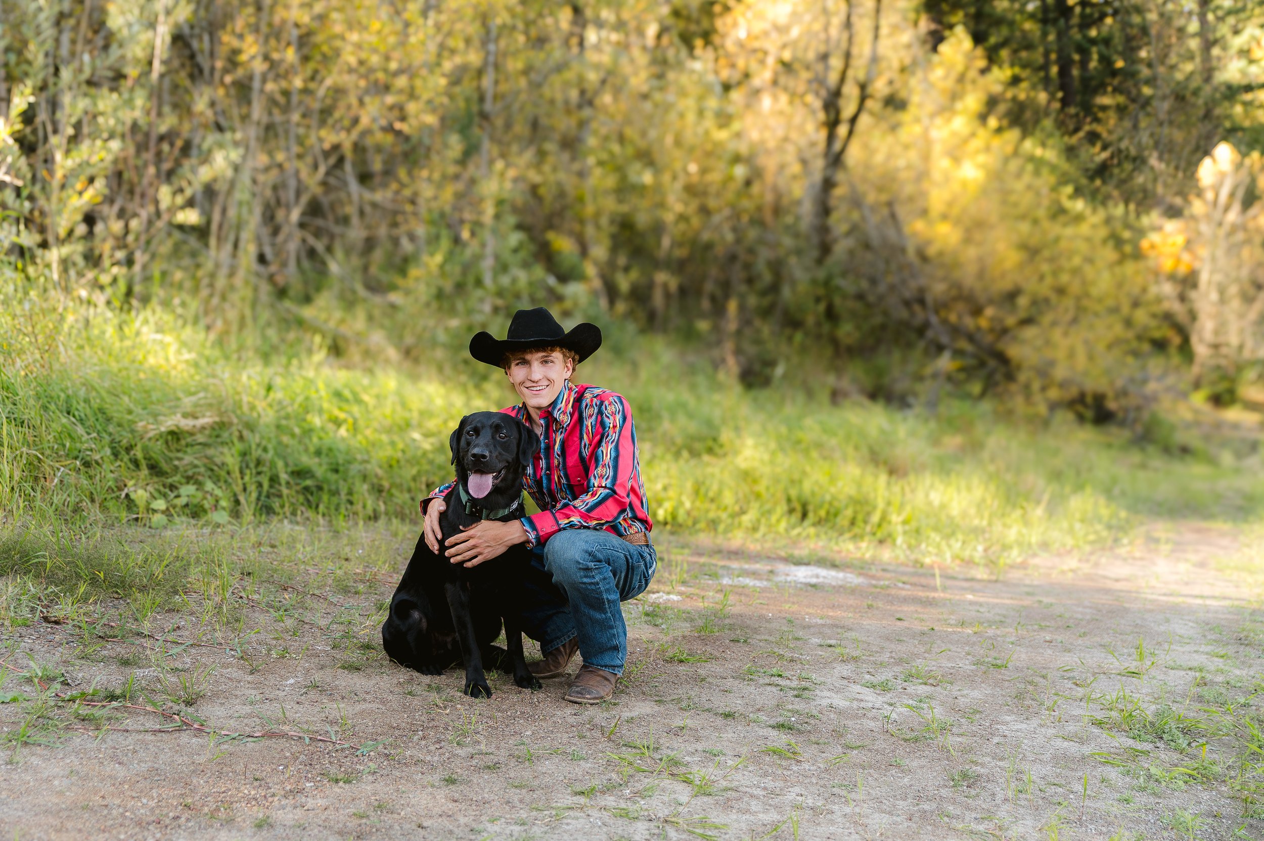 High school senior in a cowboy hat posing with his dog during an outdoor senior photo session in Vancouver WA