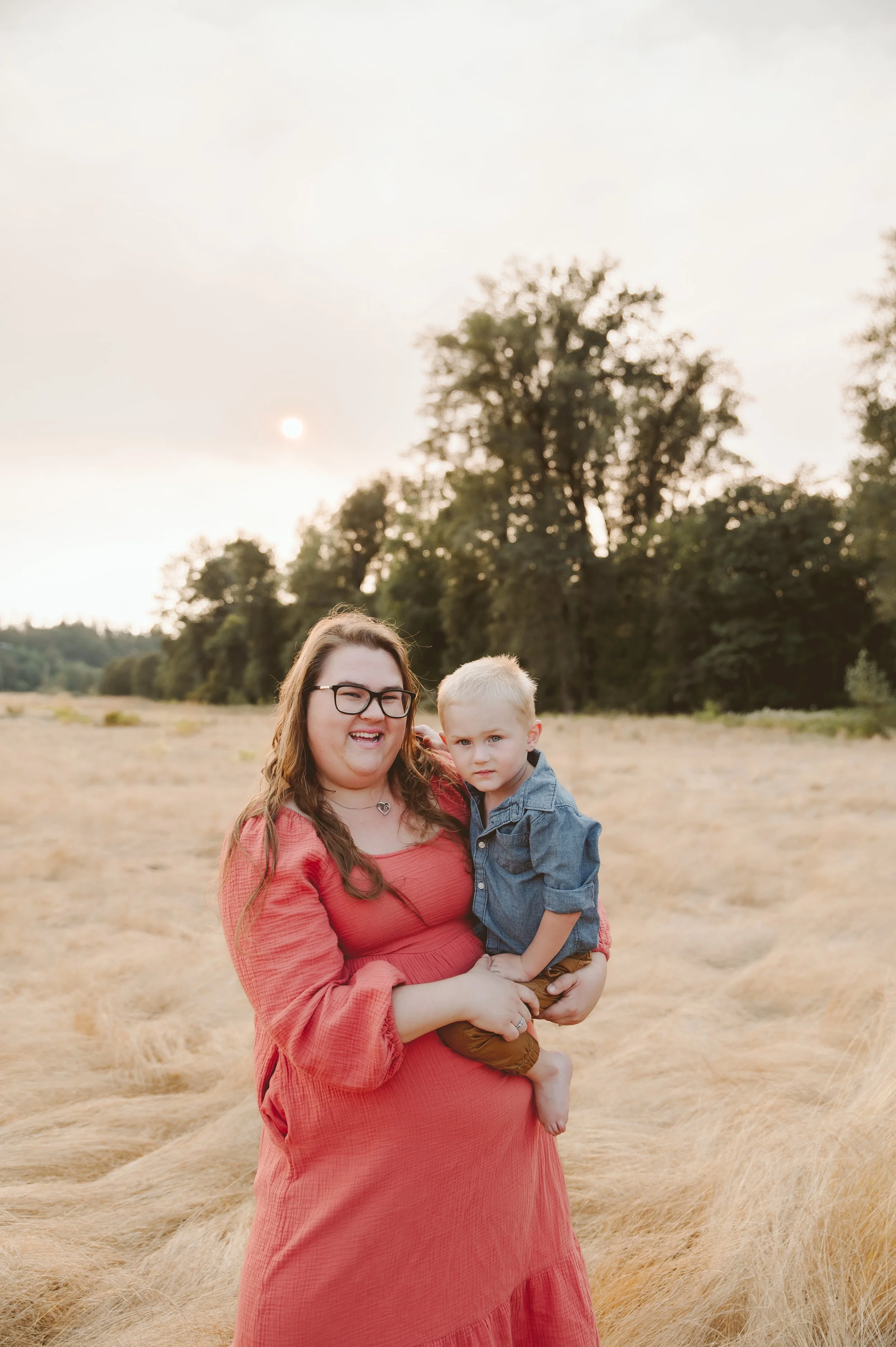 Motherhood and family photography of a woman holding her young child during sunset in an open field, captured by a Vancouver Washington family photographer.
