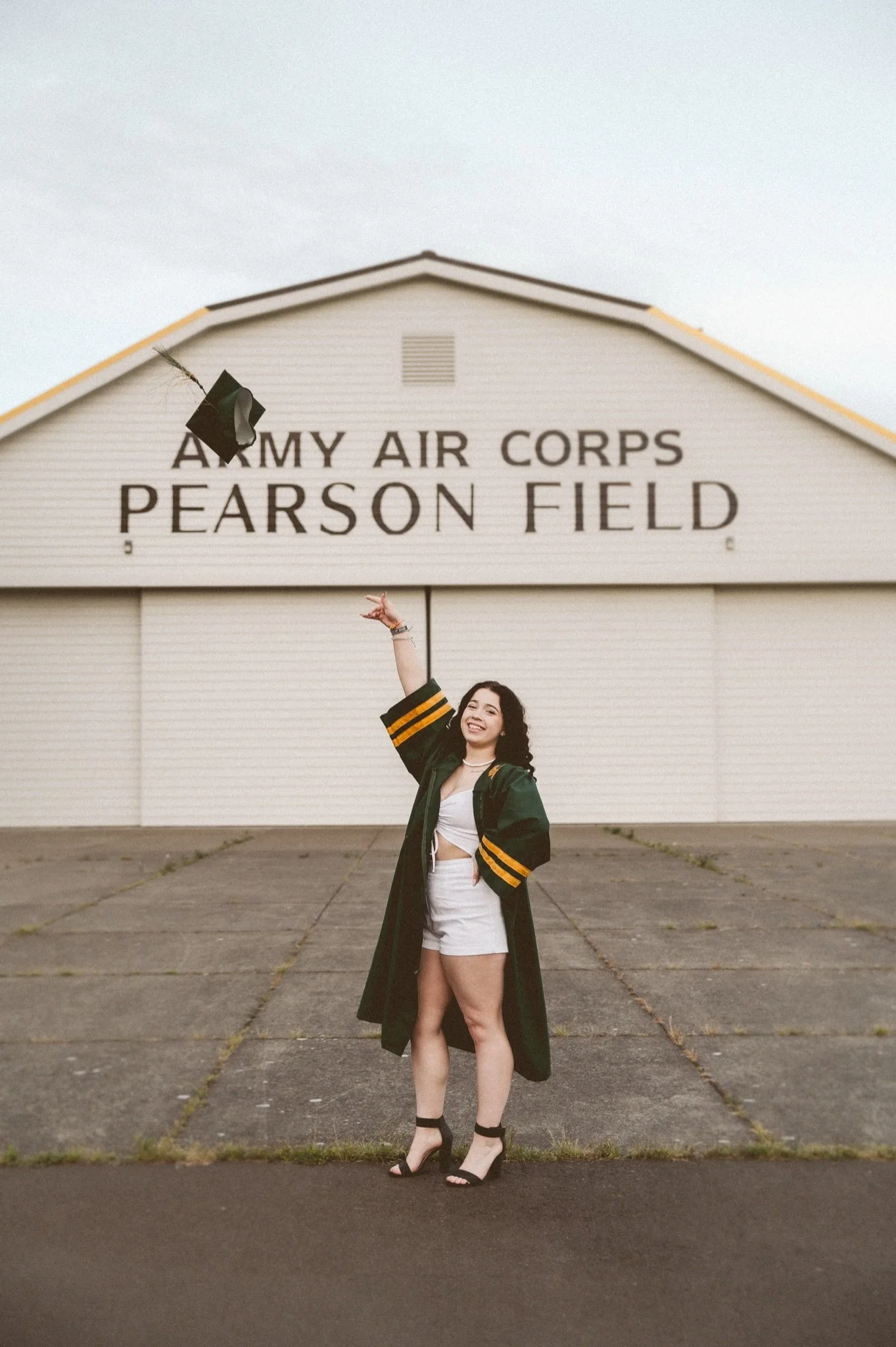 College graduate in cap and gown posing for graduation photos at Pearson Air Field in Vancouver WA