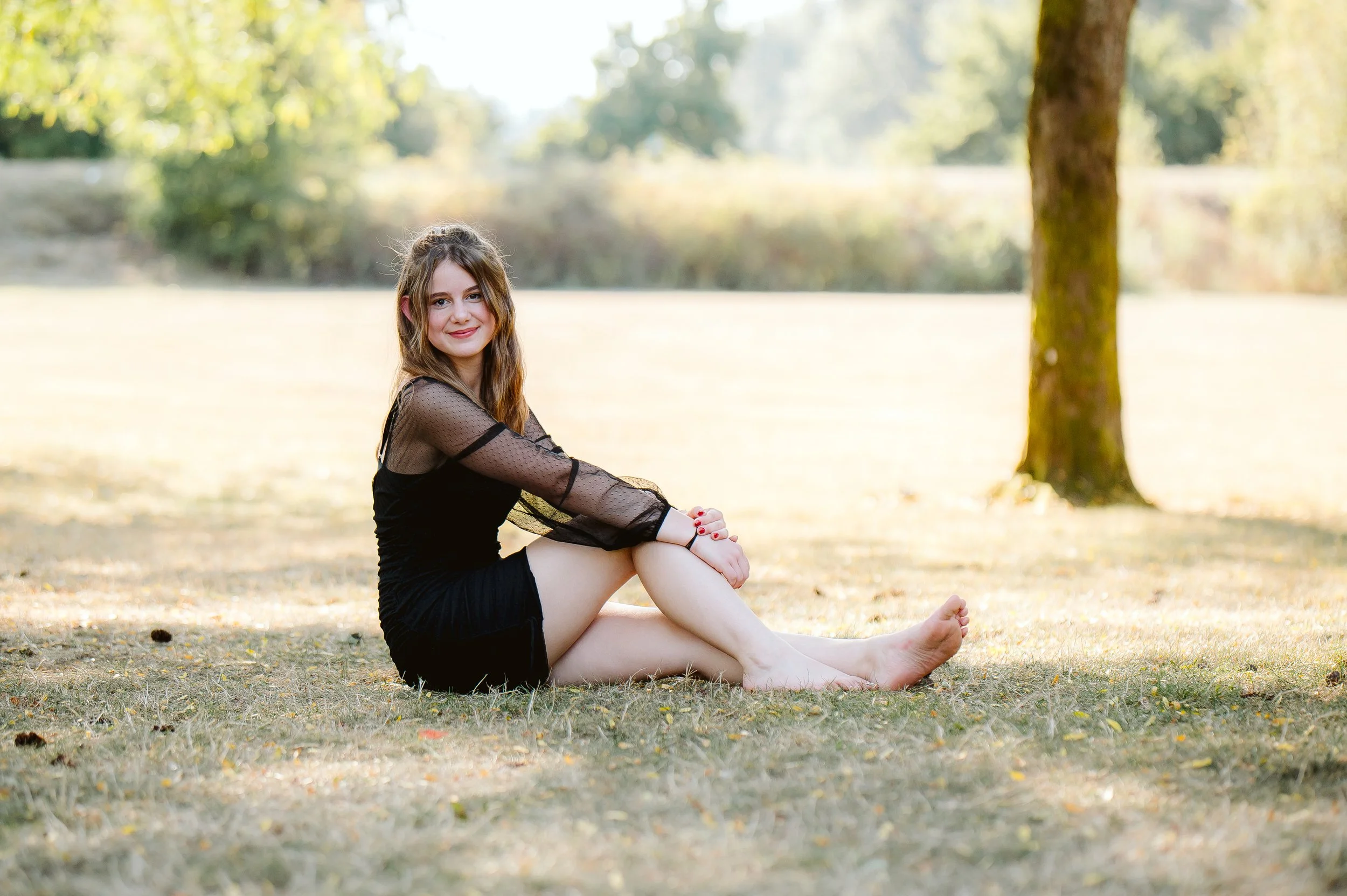 Outdoor senior portrait photographed in Vancouver Washington, featuring a relaxed seated pose in soft natural light with a warm, seasonal backdrop.
