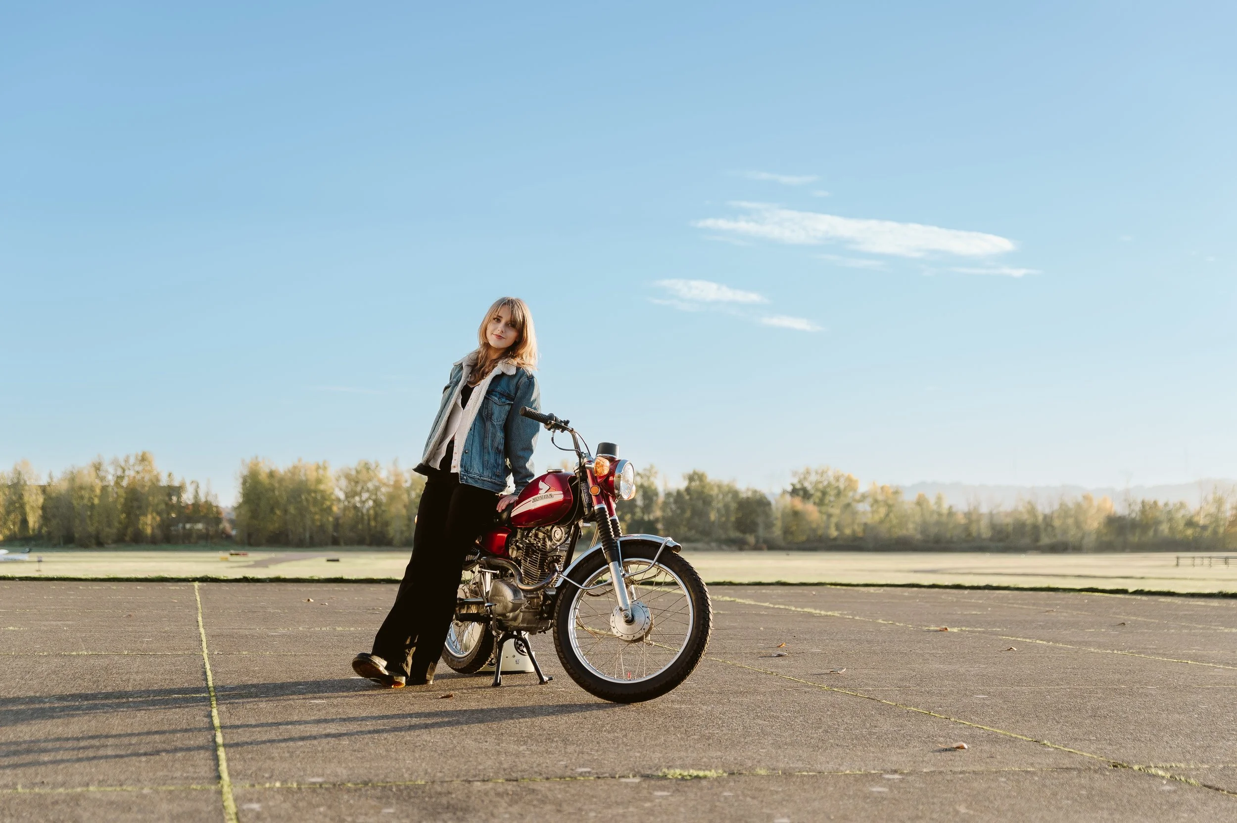 High school senior girl posing with motorcycle in open lot during editorial style senior photo session in Vancouver Washington