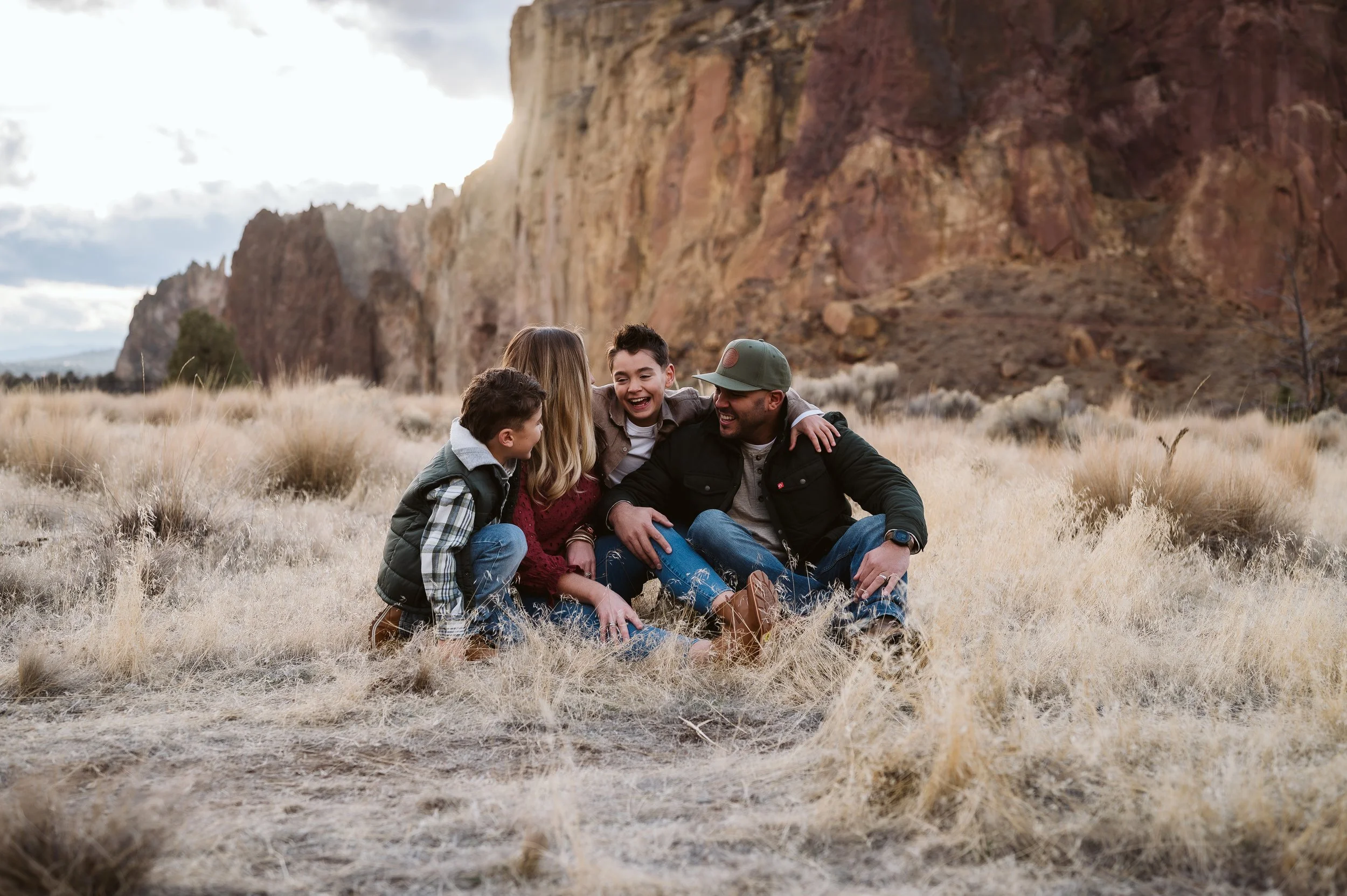 Candid family photography in Oregon capturing parents and children sitting together and interacting naturally in an outdoor setting.