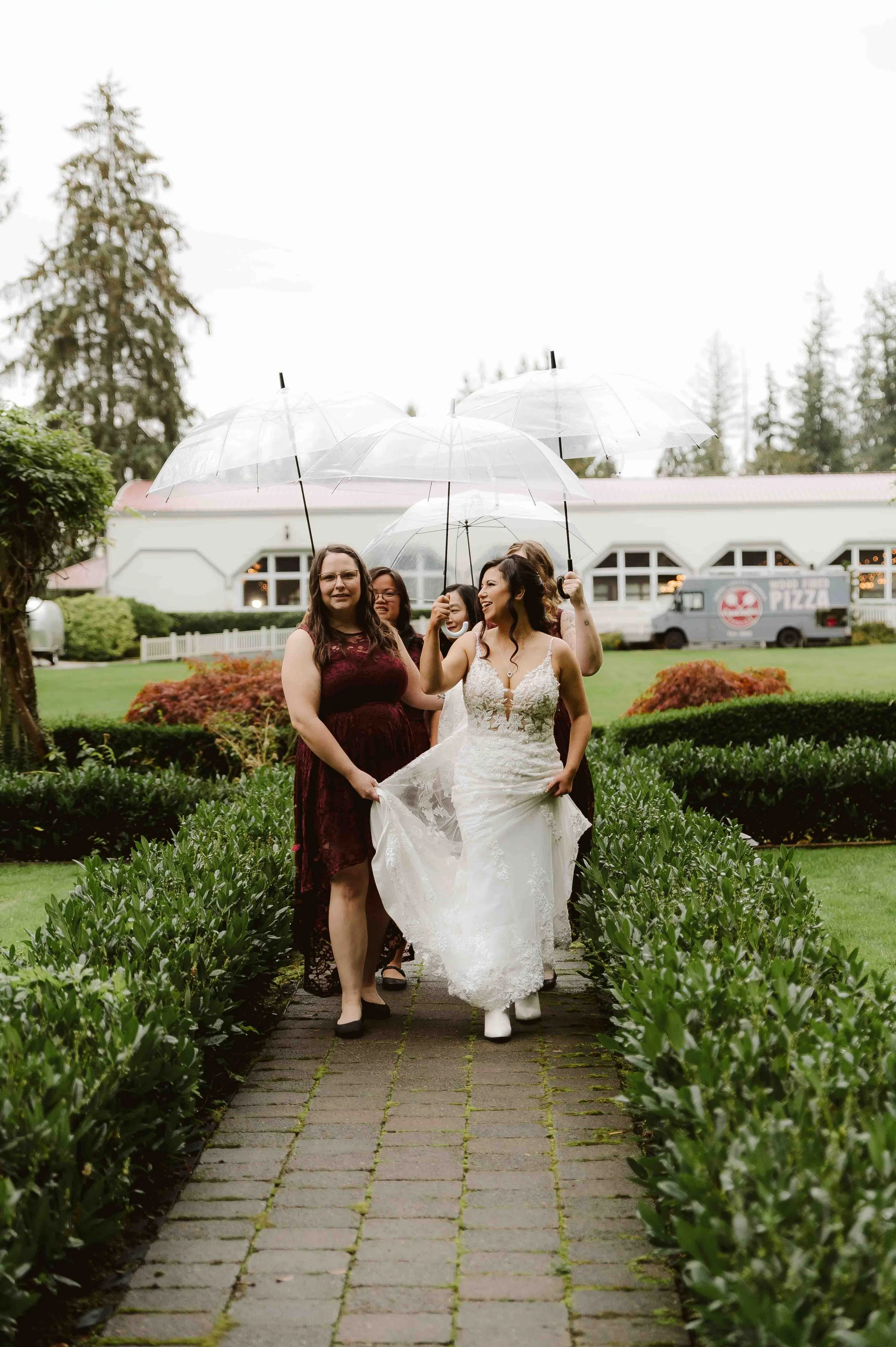 Bride and bridesmaids standing together under clear umbrellas in a garden during a rainy intimate wedding in Oregon