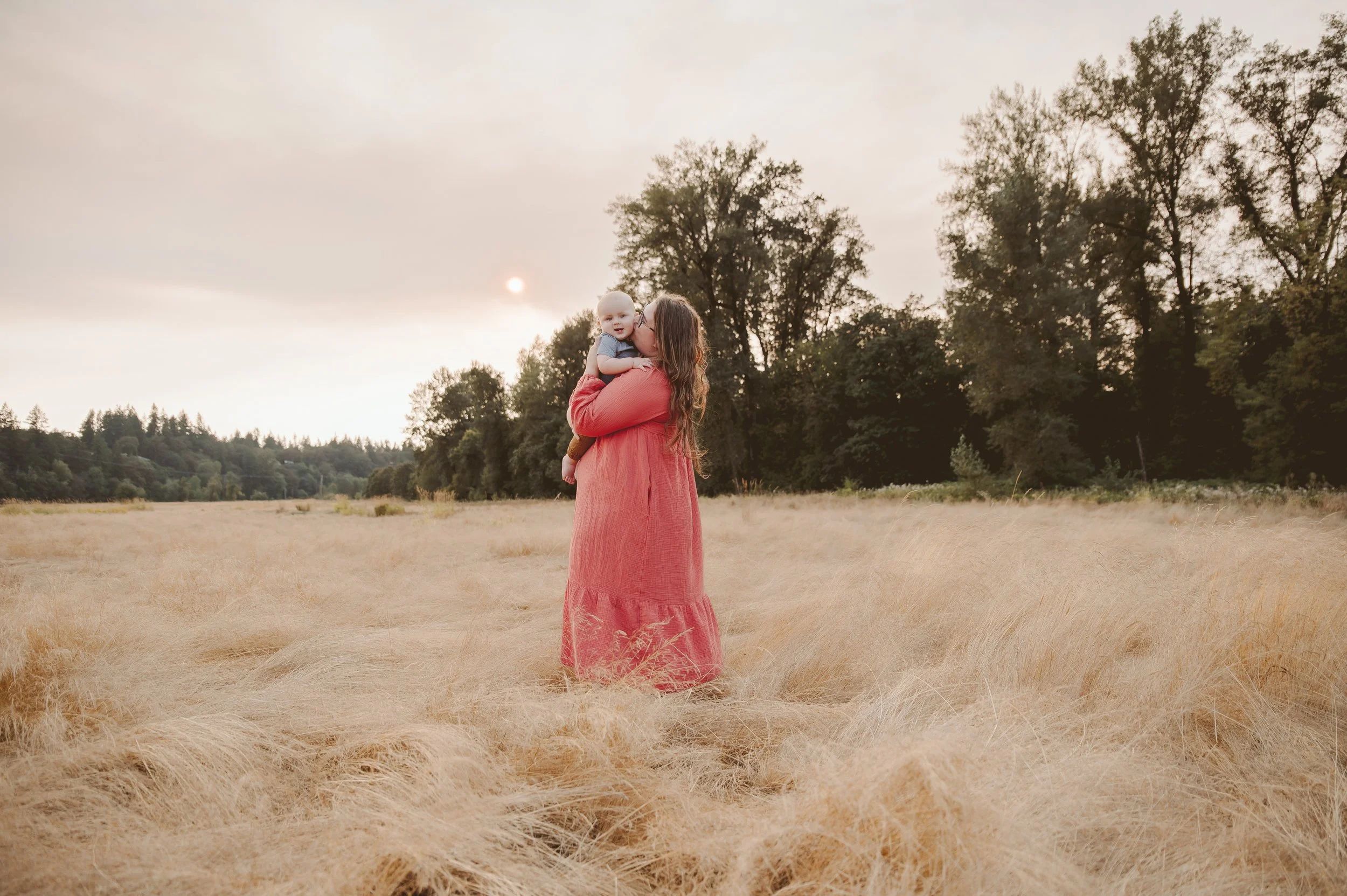 Golden hour motherhood photography of a woman holding her baby in a field of tall dry grass, photographed by a Vancouver Washington family photographer.
