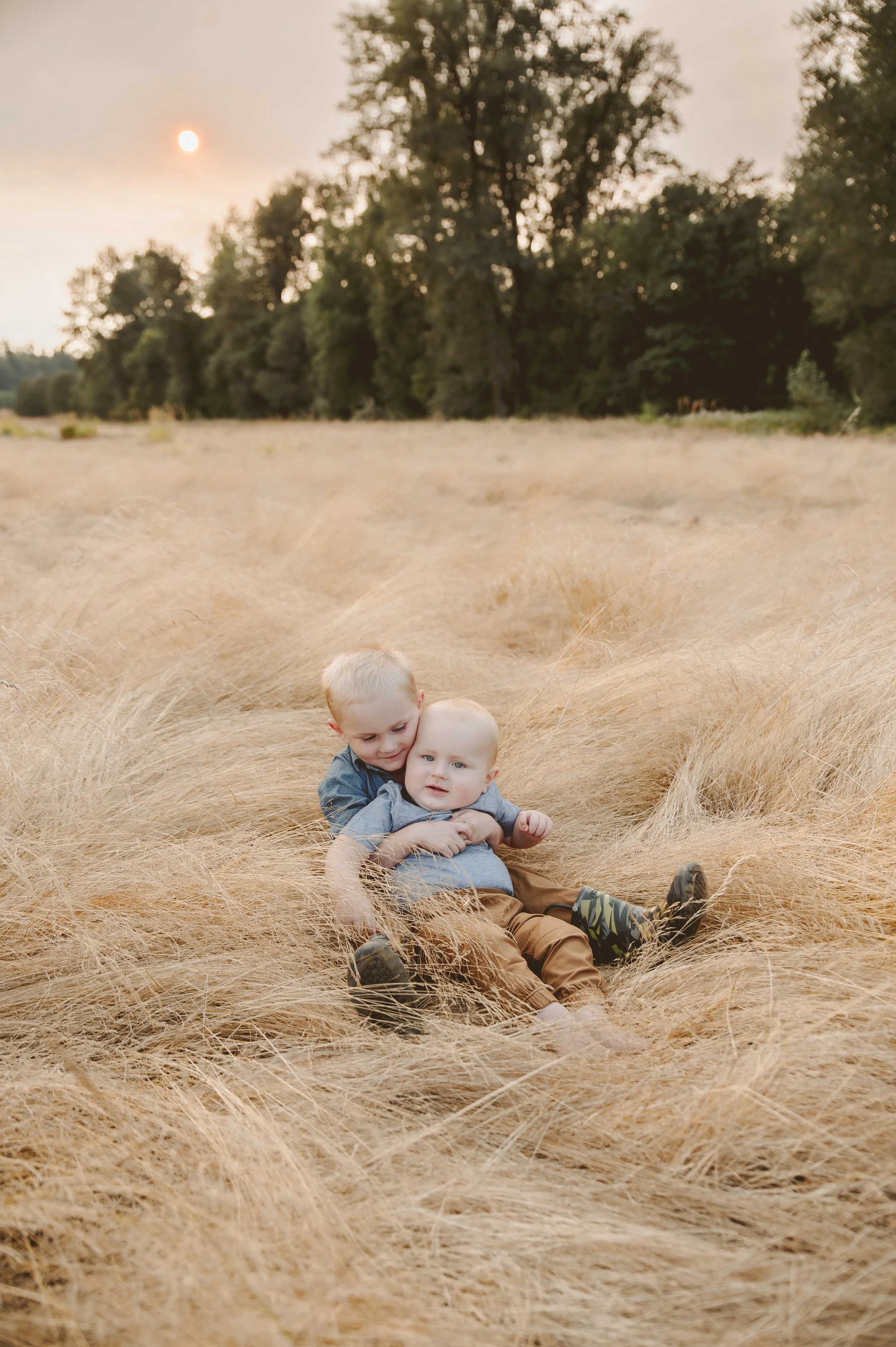Outdoor family photography of two young children sitting in tall golden grass, captured by a Vancouver Washington photographer in a natural field setting.
