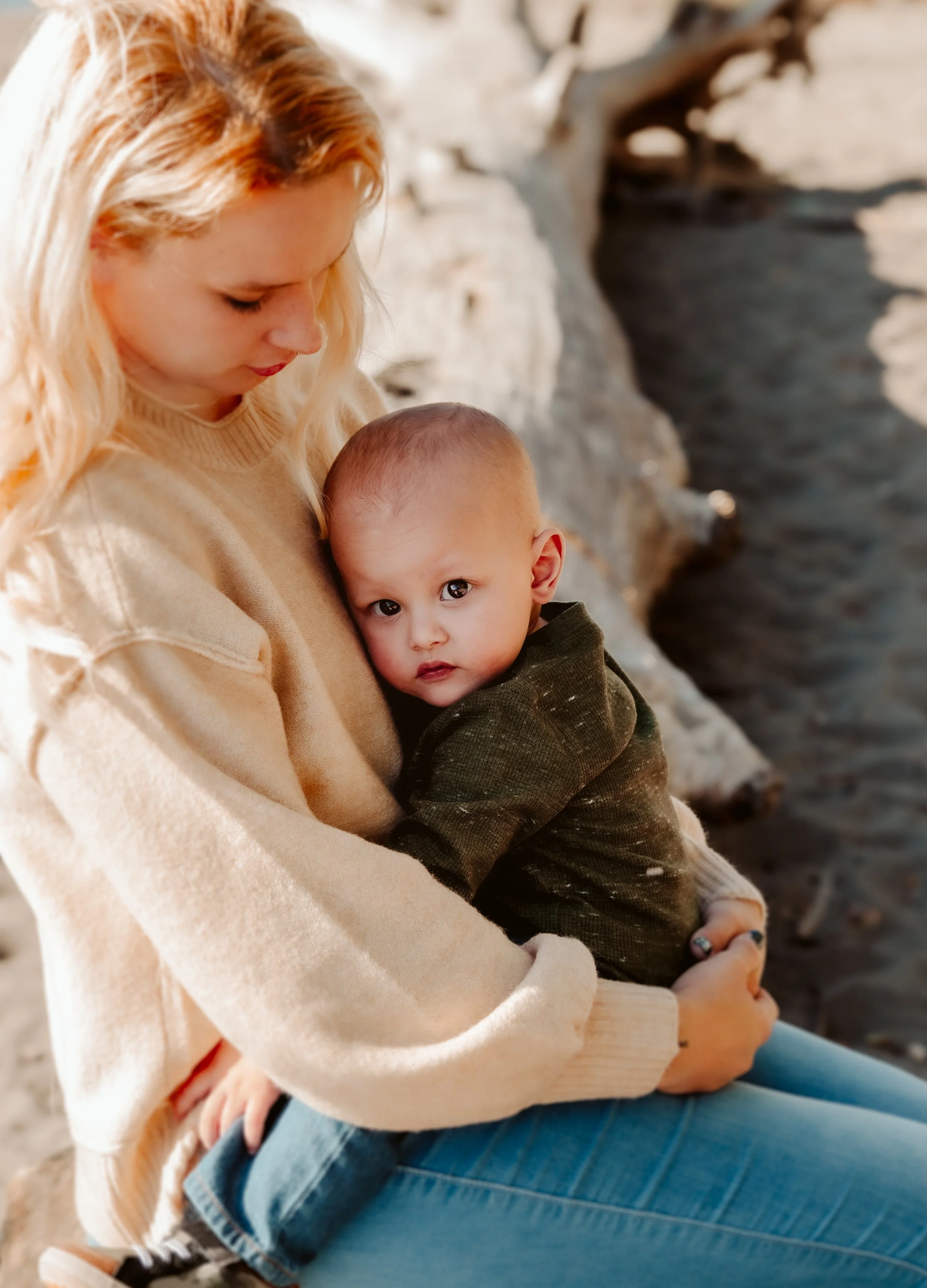 A woman holding a young child near a rocky shoreline with water in the background.