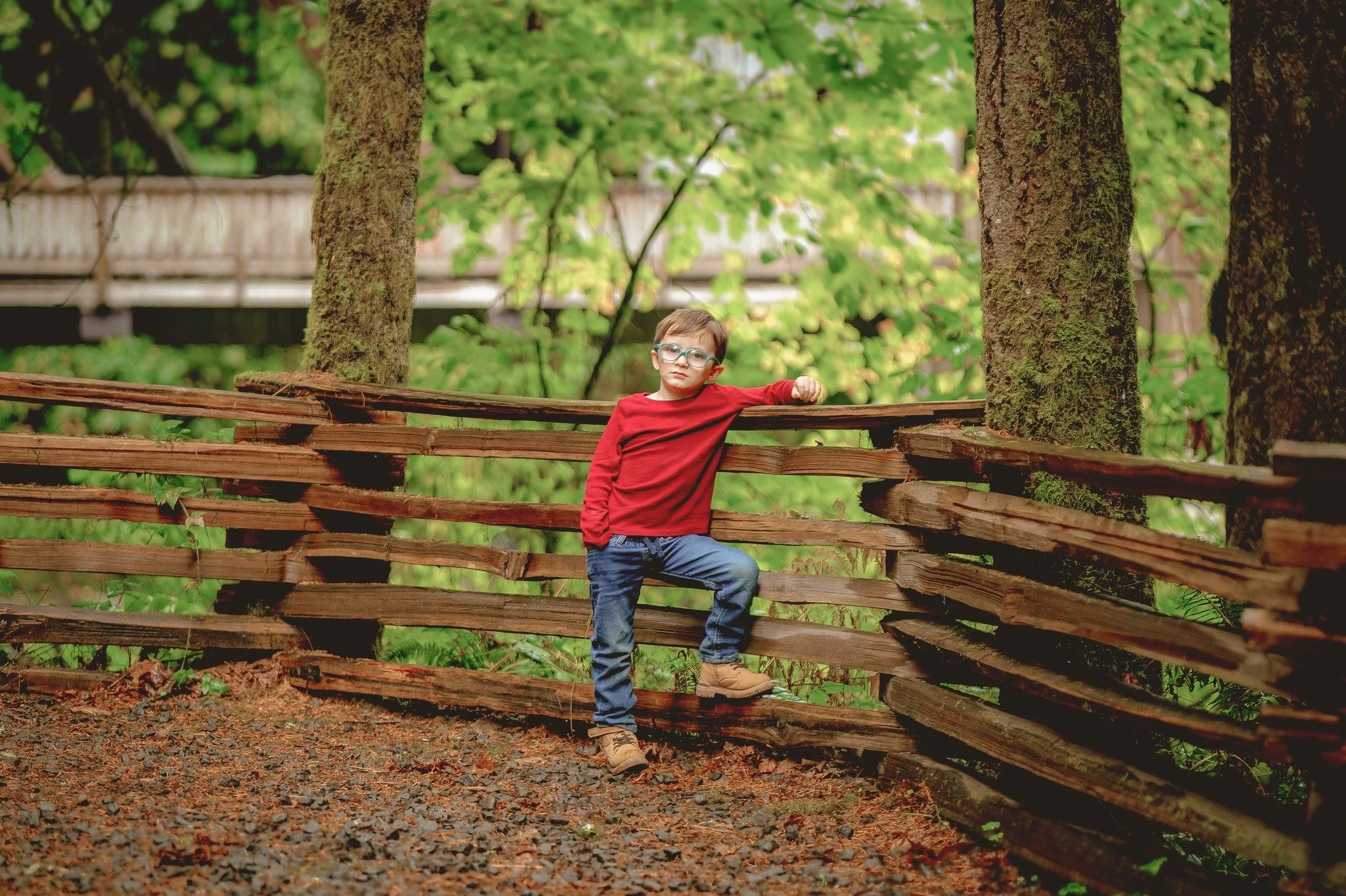 Child standing near a wooden fence in lush green spring scenery during a Vancouver Washington outdoor family photography session